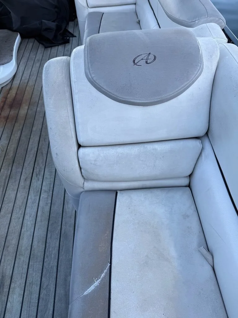 A white boat seat with a gray cushioned headrest, showing some dirt and wear, on a wooden deck with a black bag nearby.