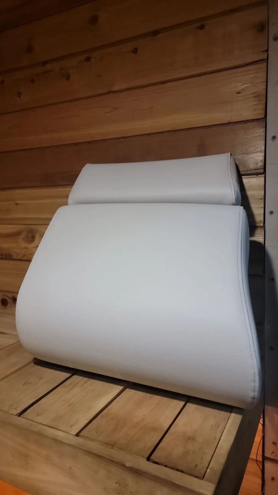 White leather chair with a padded headrest, placed on a wooden surface against a wooden wall.