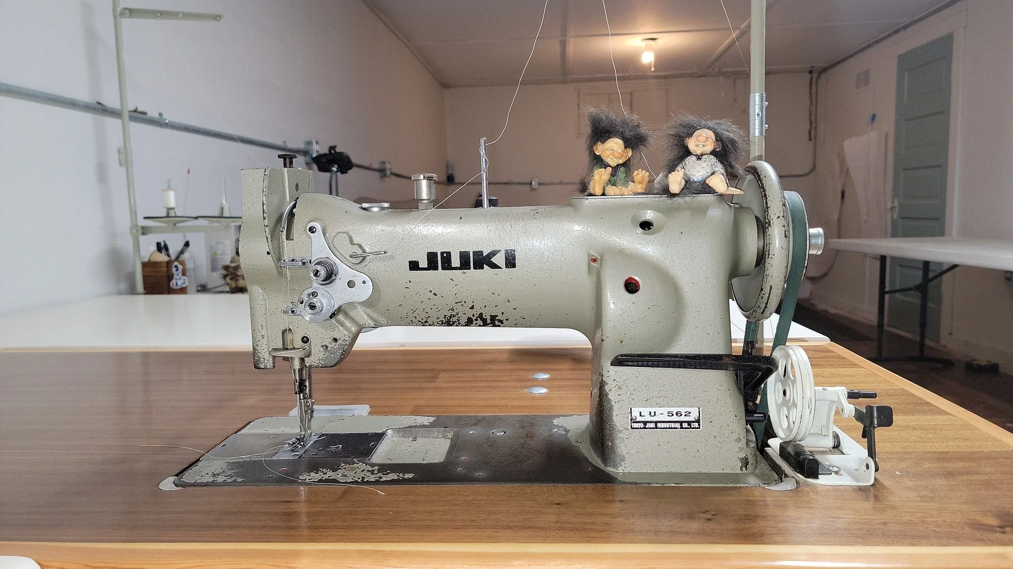 An old Janome industrial sewing machine on a wooden table with two small troll dolls on top.