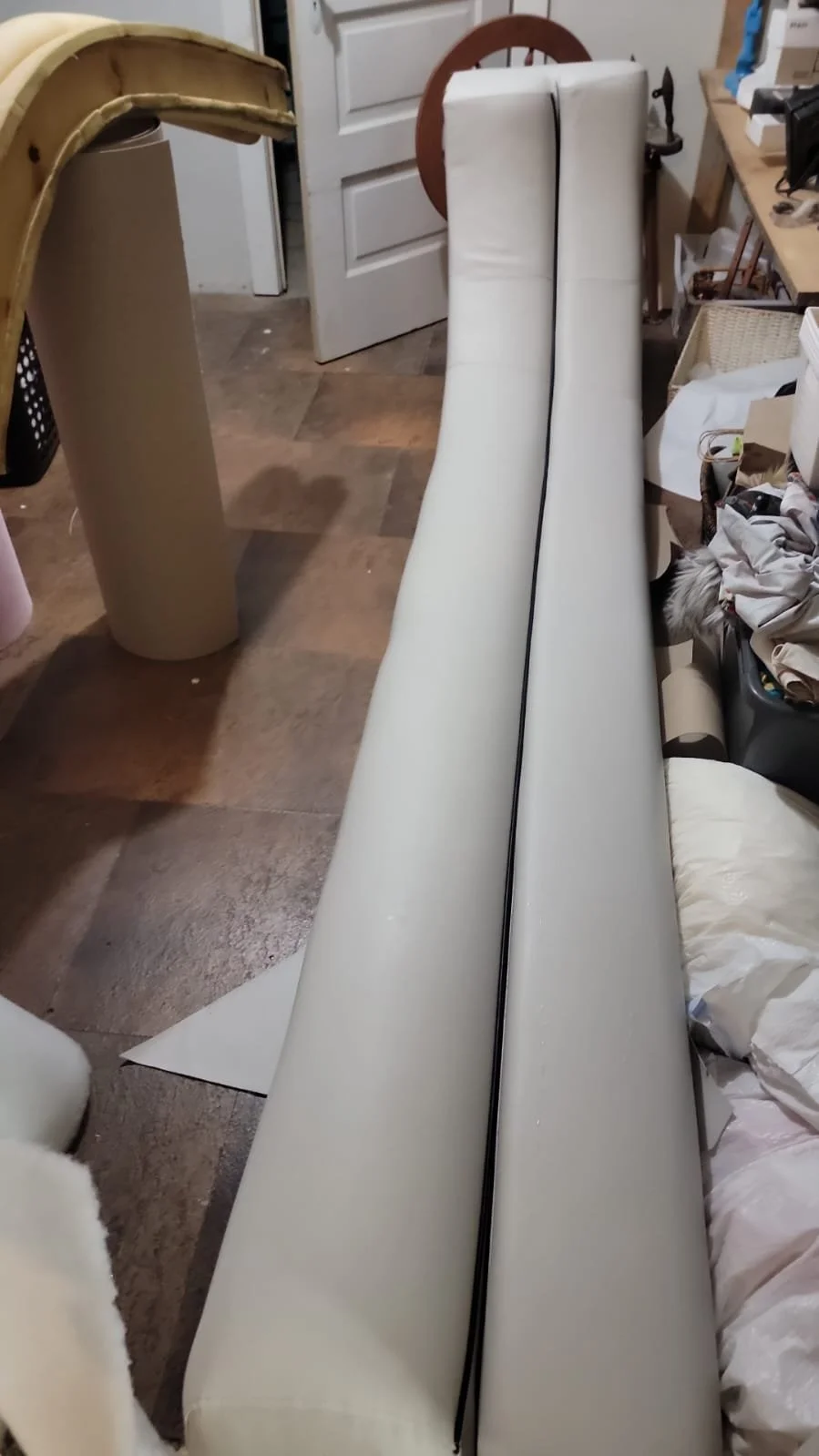 Two white hospital or medical examination tables or stretchers, placed side by side, in a cluttered room with various furniture and items around.