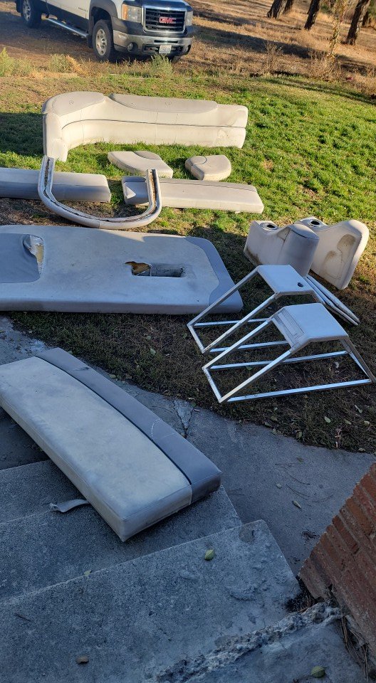 Disassembled boat seats and parts laid out on grass and concrete outdoors, with a pickup truck in the background.