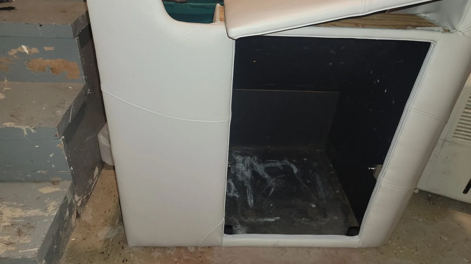 Empty white leather-piece lounge chair or booth with black interior and some white scuff marks, placed beside worn gray wooden stairs.