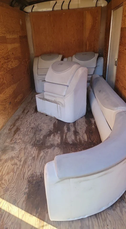 Several white upholstered chairs, including two armchairs and three hidden chairs, are stored inside a small wooden room with plywood walls and a wooden floor.