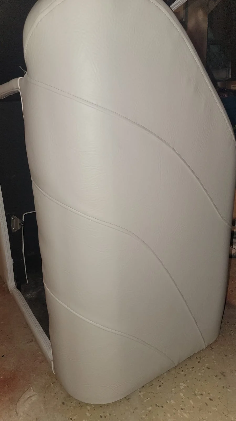 The image shows the side view of a white leather upholstered recliner chair, with some visible stitching details, placed on a beige tiled floor.