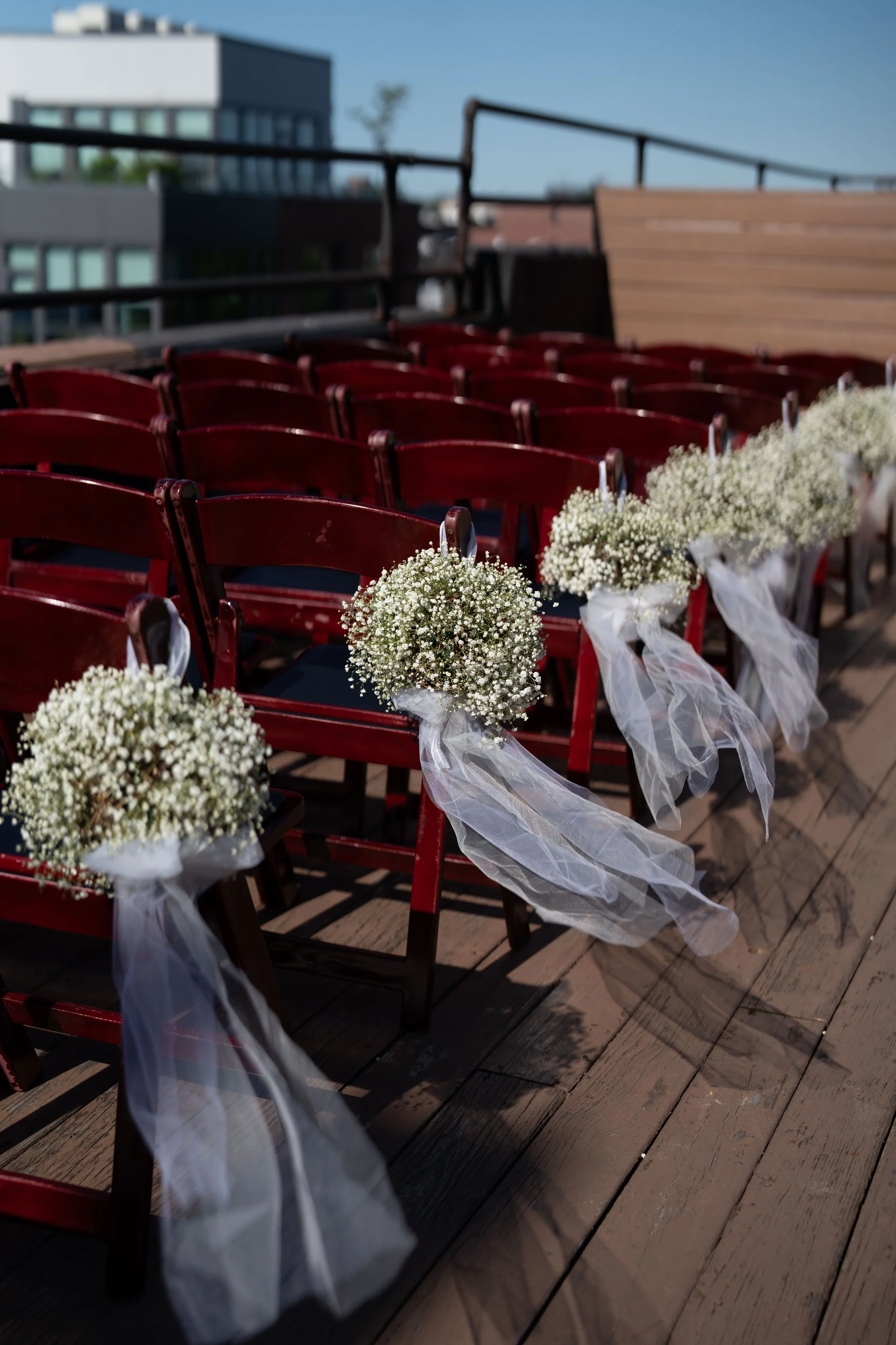 Wedding chairs decorated with white baby's breath flowers and white tulle bows on an outdoor wooden deck.