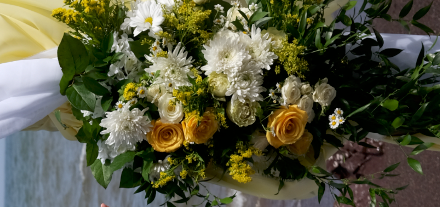 A bouquet of white, yellow, and green flowers including roses, daisies, and other blossoms with green leaves, which appears to be a floral arrangement for a special occasion.