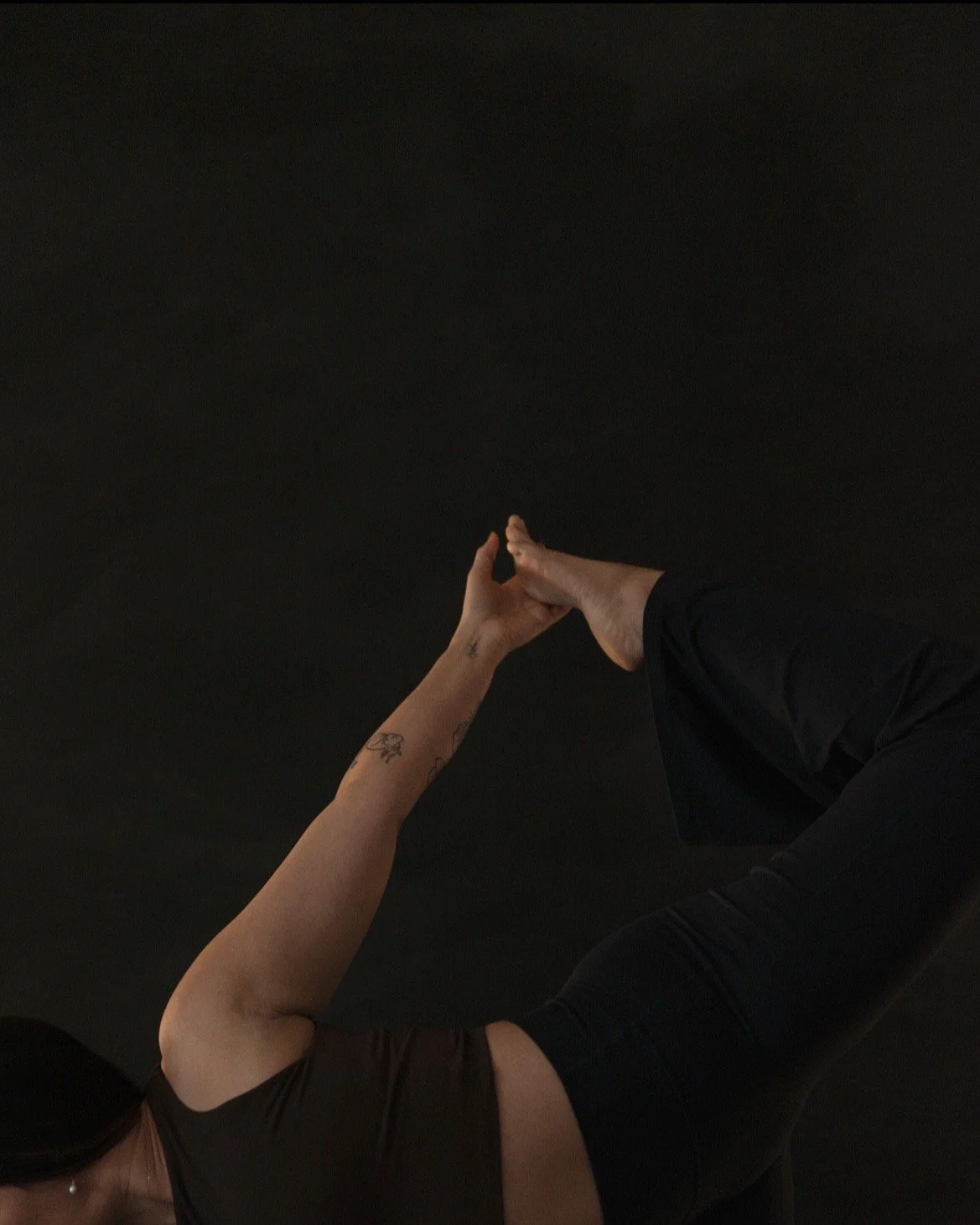 Person performing a handstand with hands touching and legs extended upward against a black background.