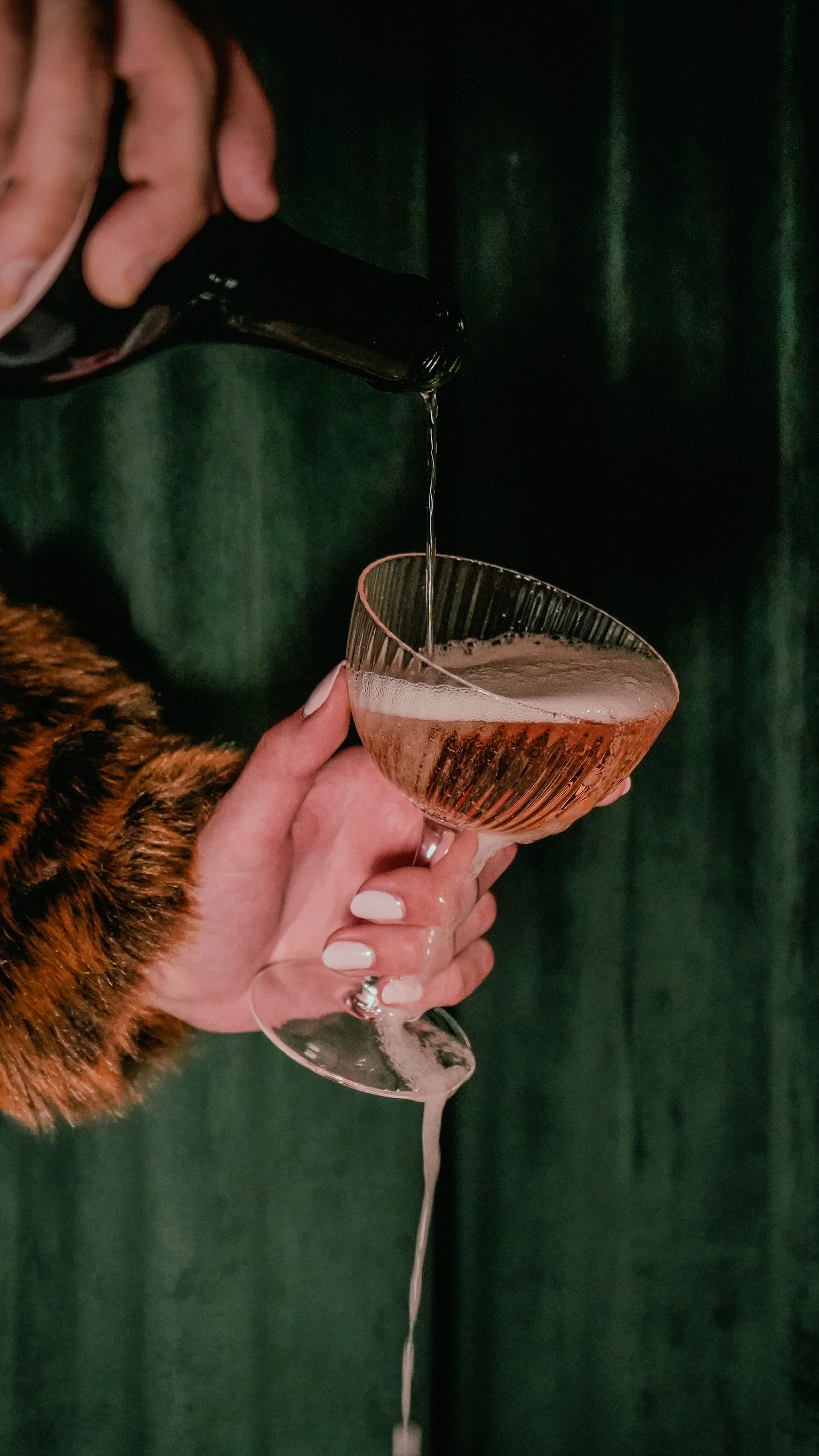 Close-up of a guest holding a crystal flute of sparkling wine as it overflows, capturing the celebratory and lively adult dining atmosphere at Viv and Jules in Hoboken.