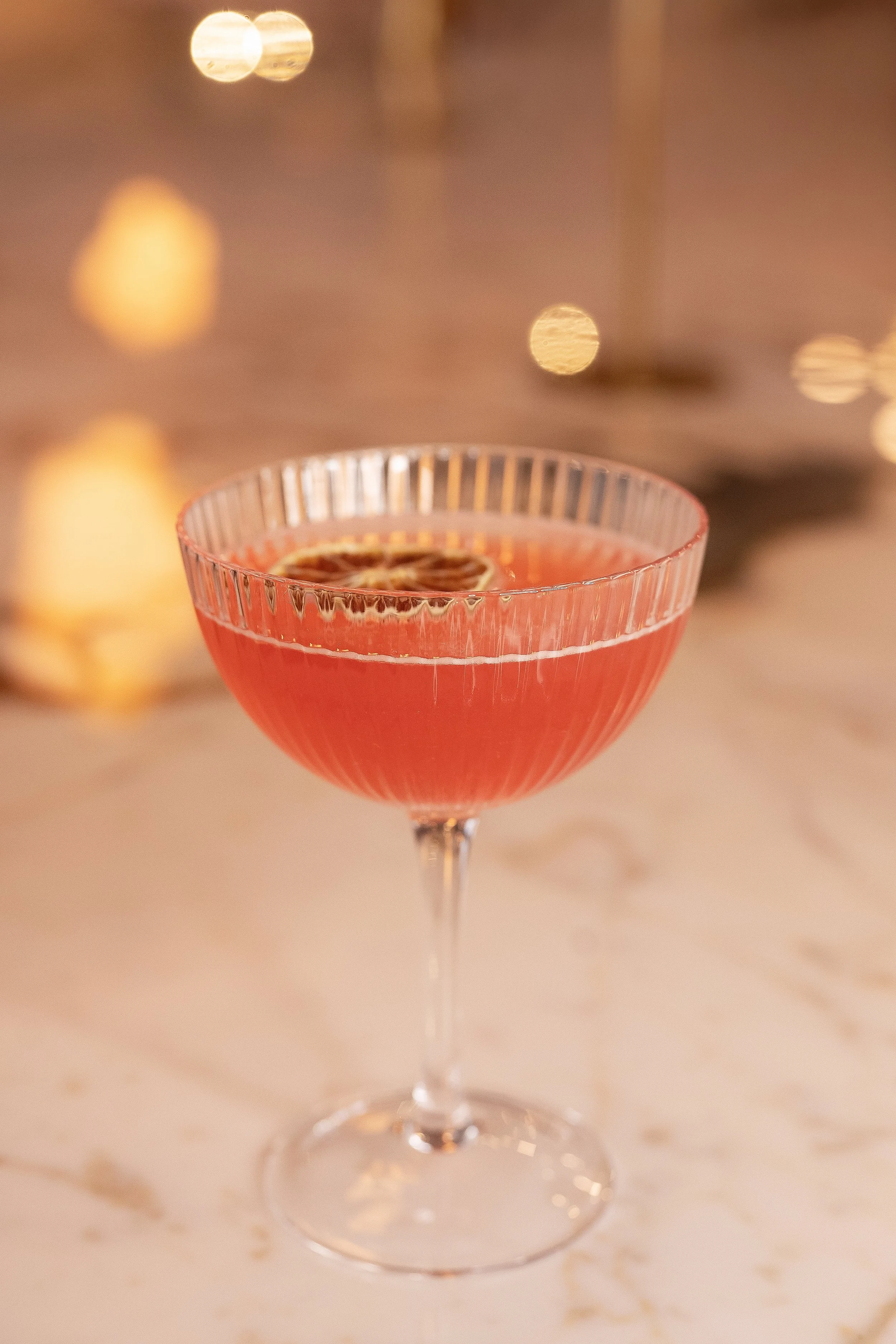 A refreshing pink citrus craft cocktail with a dried grapefruit garnish, served in a fluted coupe glass at the Viv & Jules bar in Hoboken.