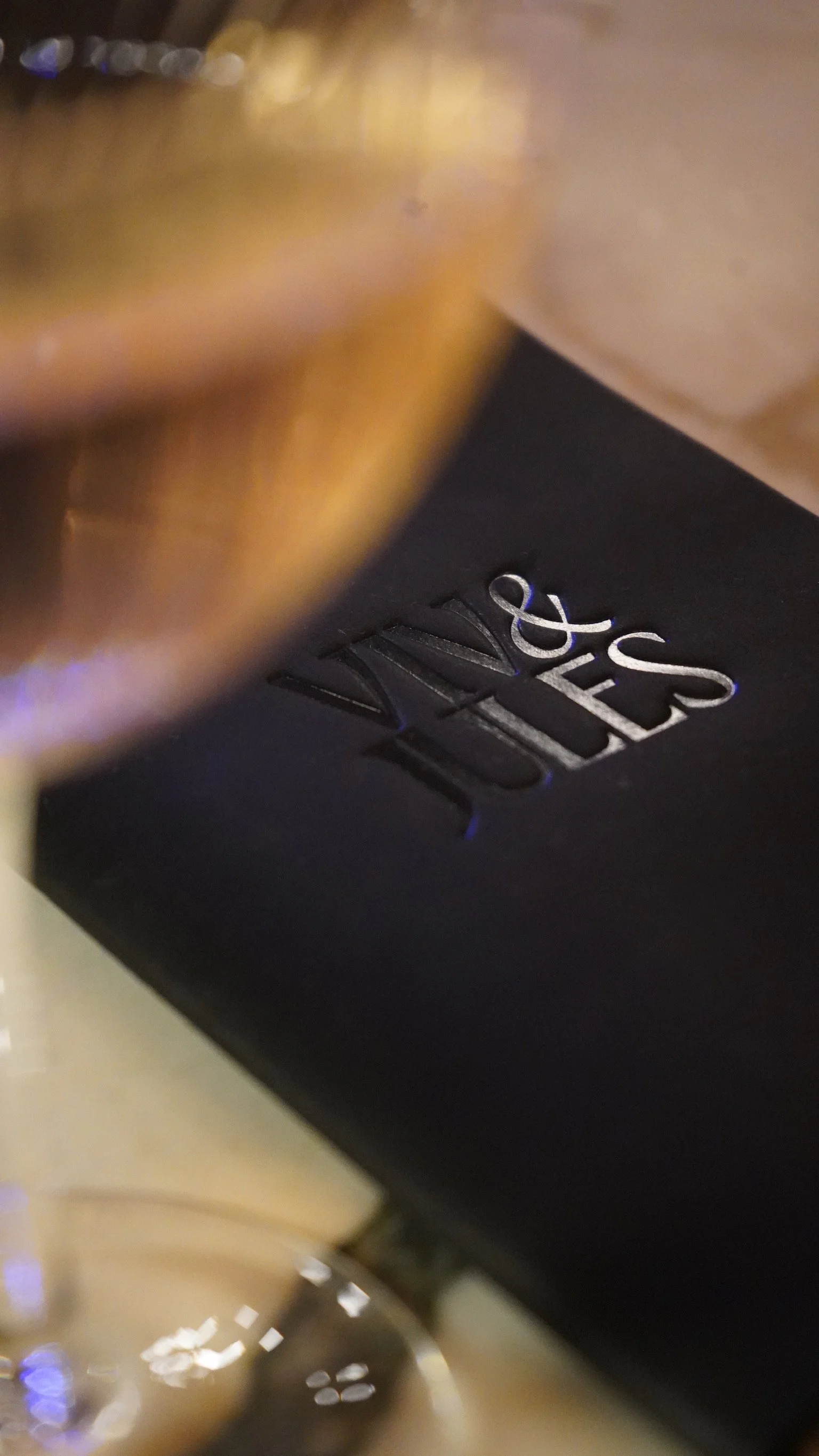 Macro detail of the Viv & Jules logo elegantly debossed on a premium black leather check presenter, reflecting the sophisticated and tactile adult dining experience in Hoboken.