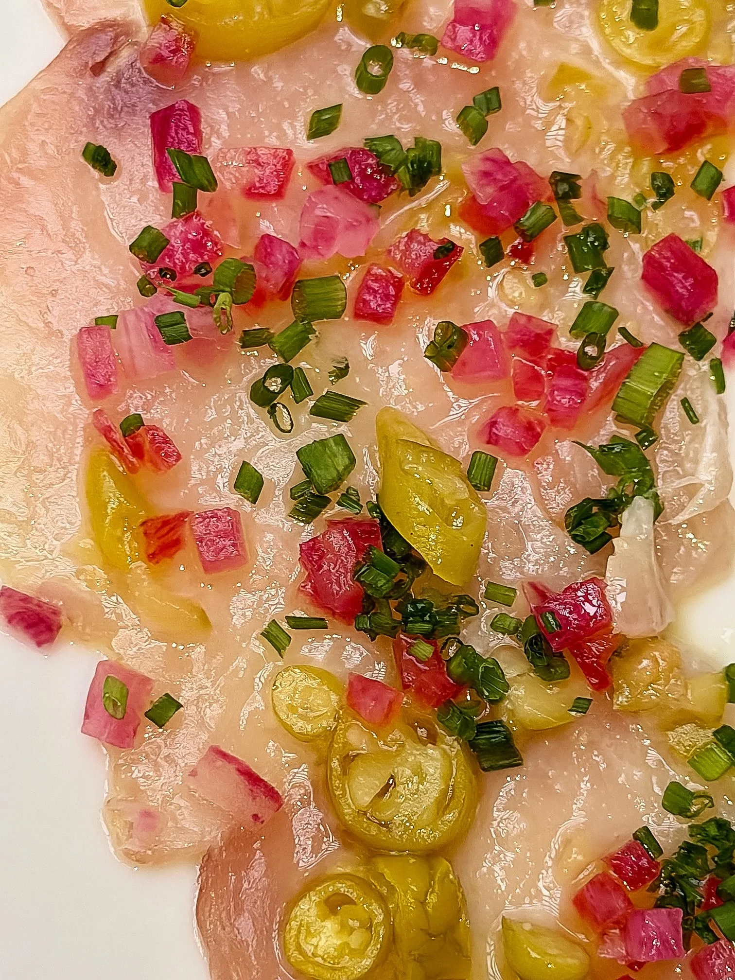 Macro shot of Hamachi Carpaccio highlighting the piparra pepper, green olive relish, and watermelon radish garnish.