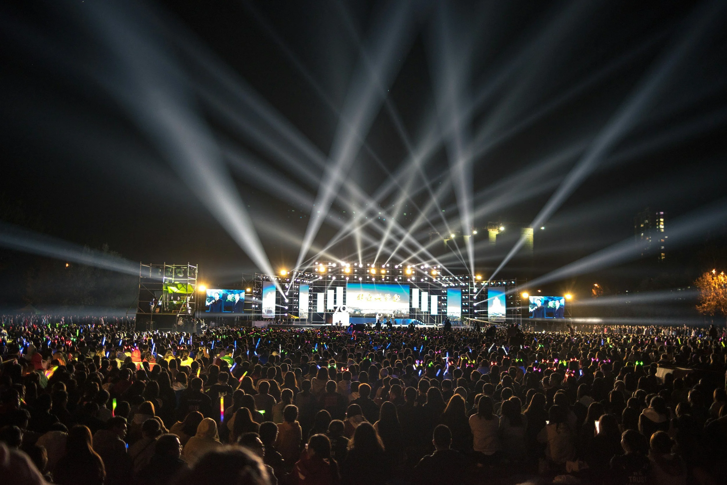 Crowd watching a live concert at night with stage lights and large screens