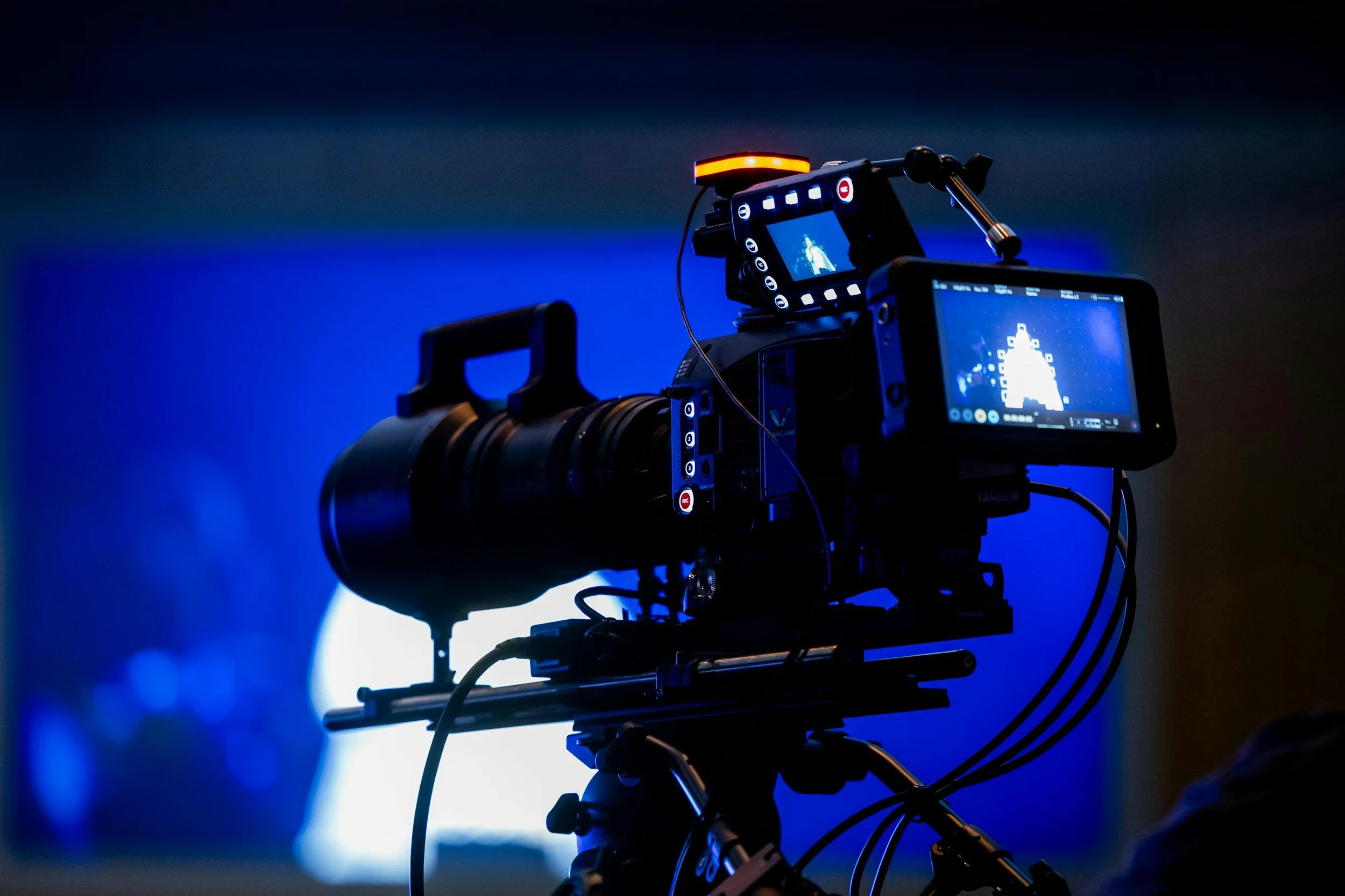 Professional video camera setup with monitors and controls, recording a scene against a dark background with blue lighting.
