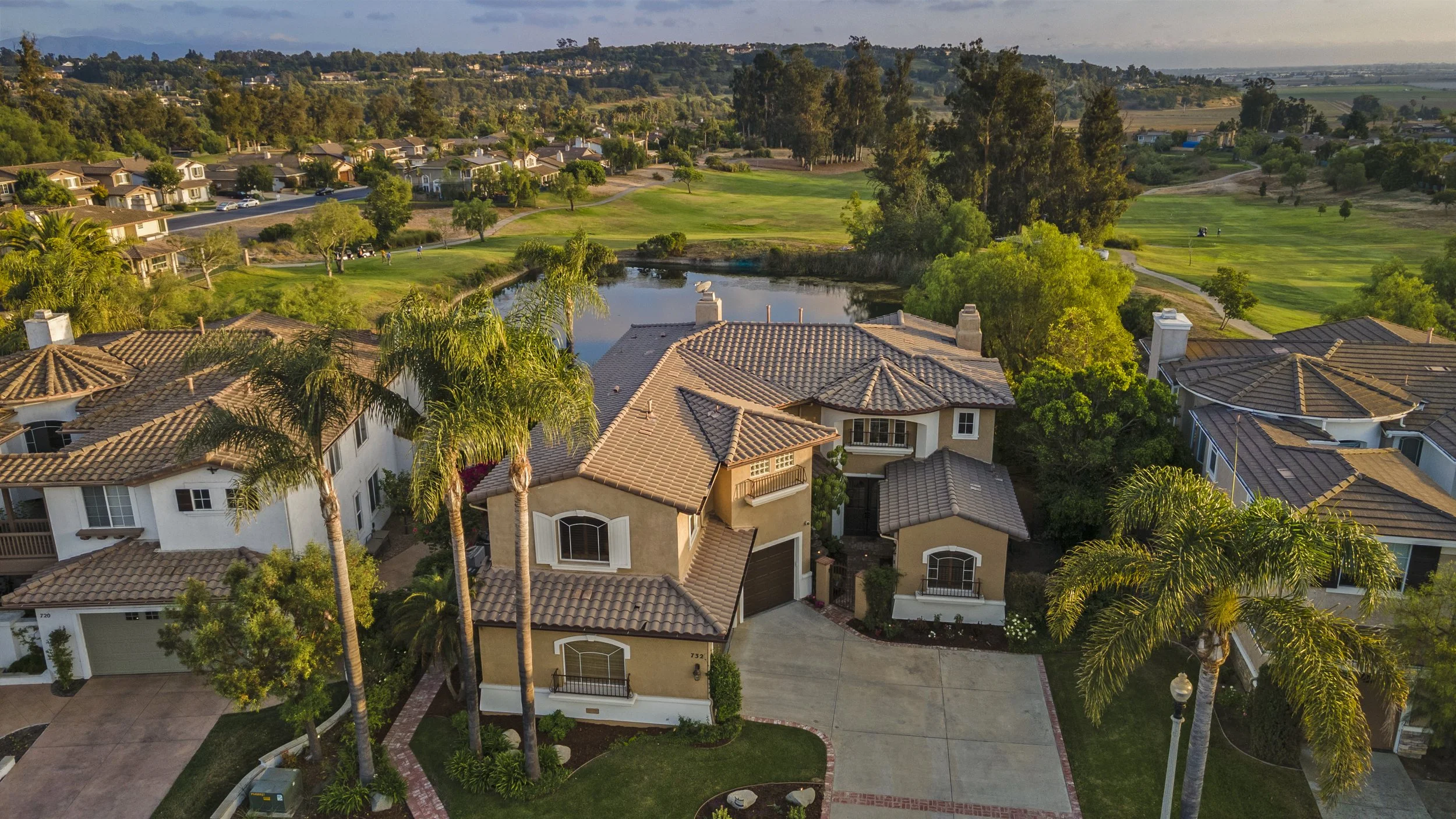Aerial view of a residential neighborhood with houses and a golf course, including a pond and green fairways, during daytime.