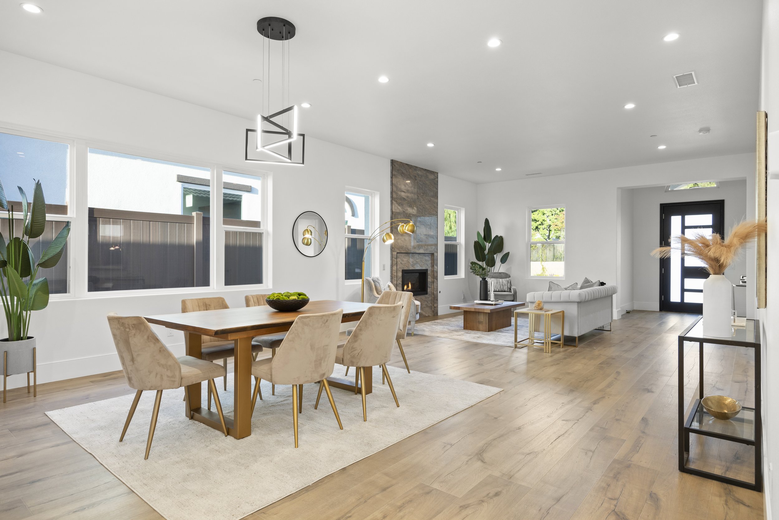 Open concept living and dining room with hardwood floors, large windows, white walls, modern furniture, a fireplace, and minimal decor.