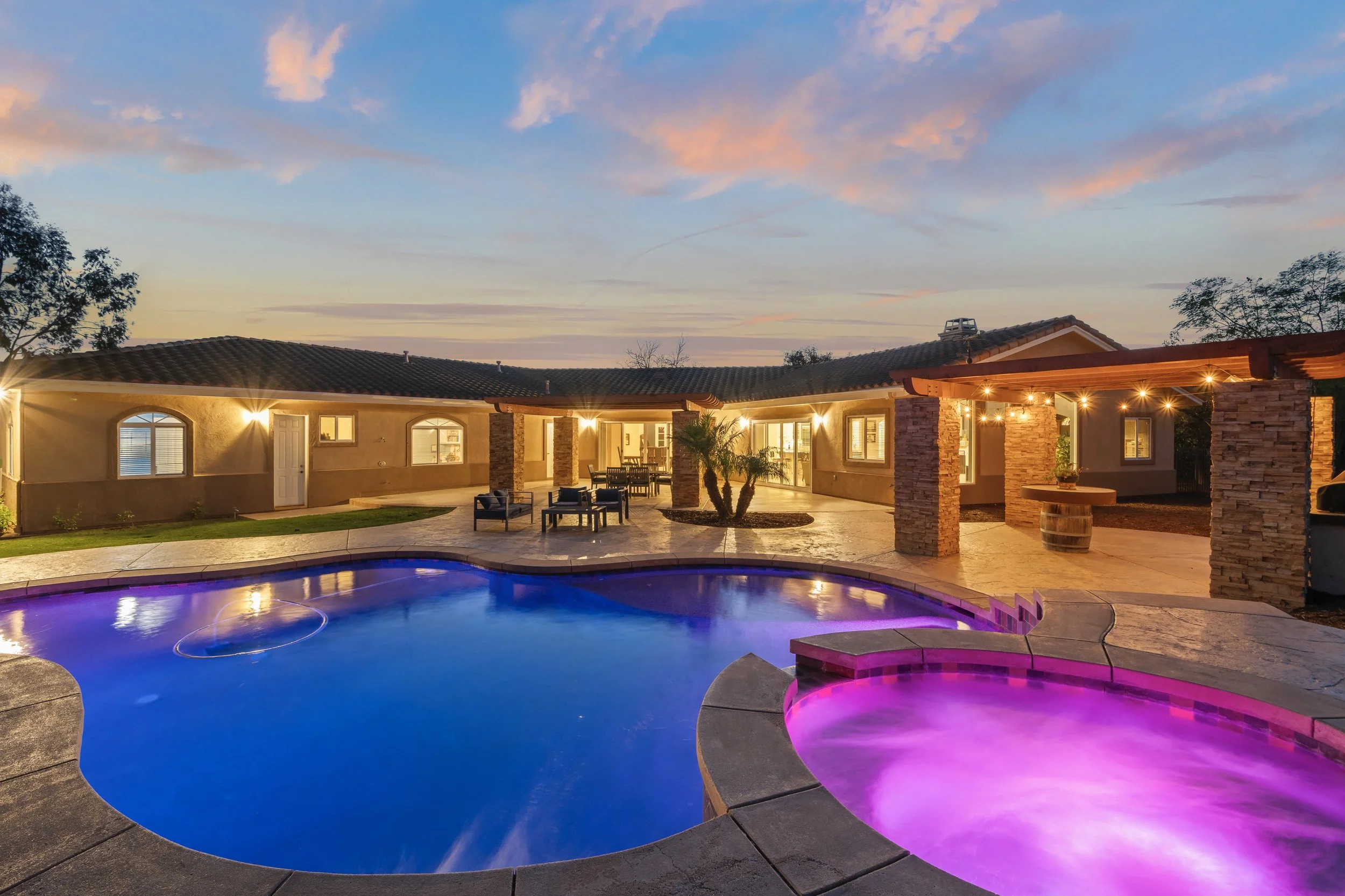 Exterior shot of a house with a pool, lit by string lights at dusk