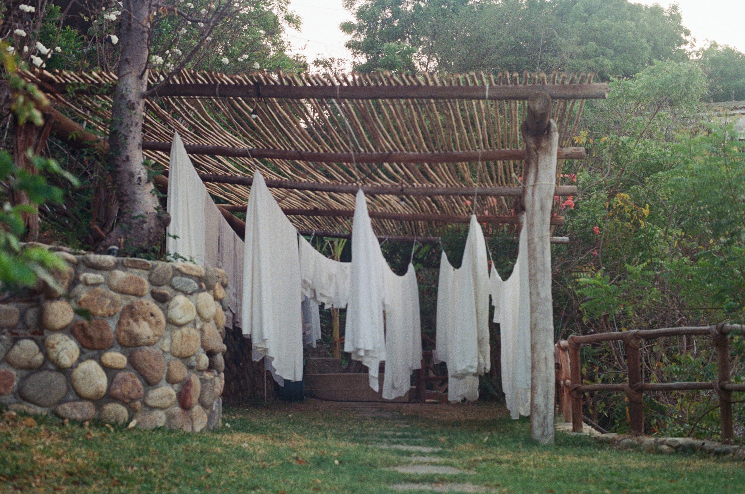 Clothes hanging on a wire outdoors, with a rustic wooden fence and trees in the background.