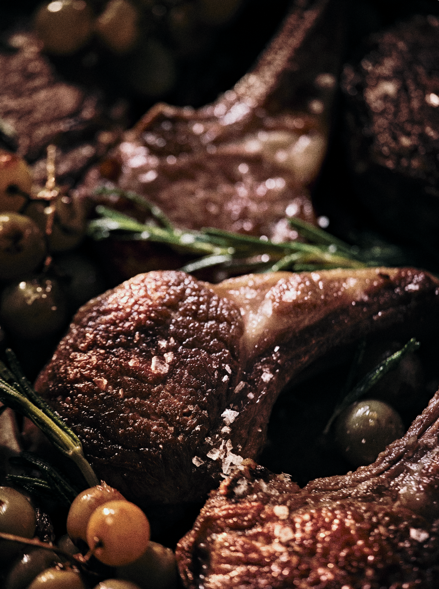 Close-up of cooked lamb chops seasoned with coarse salt, garnished with rosemary sprigs, accompanied by green and white grapes.