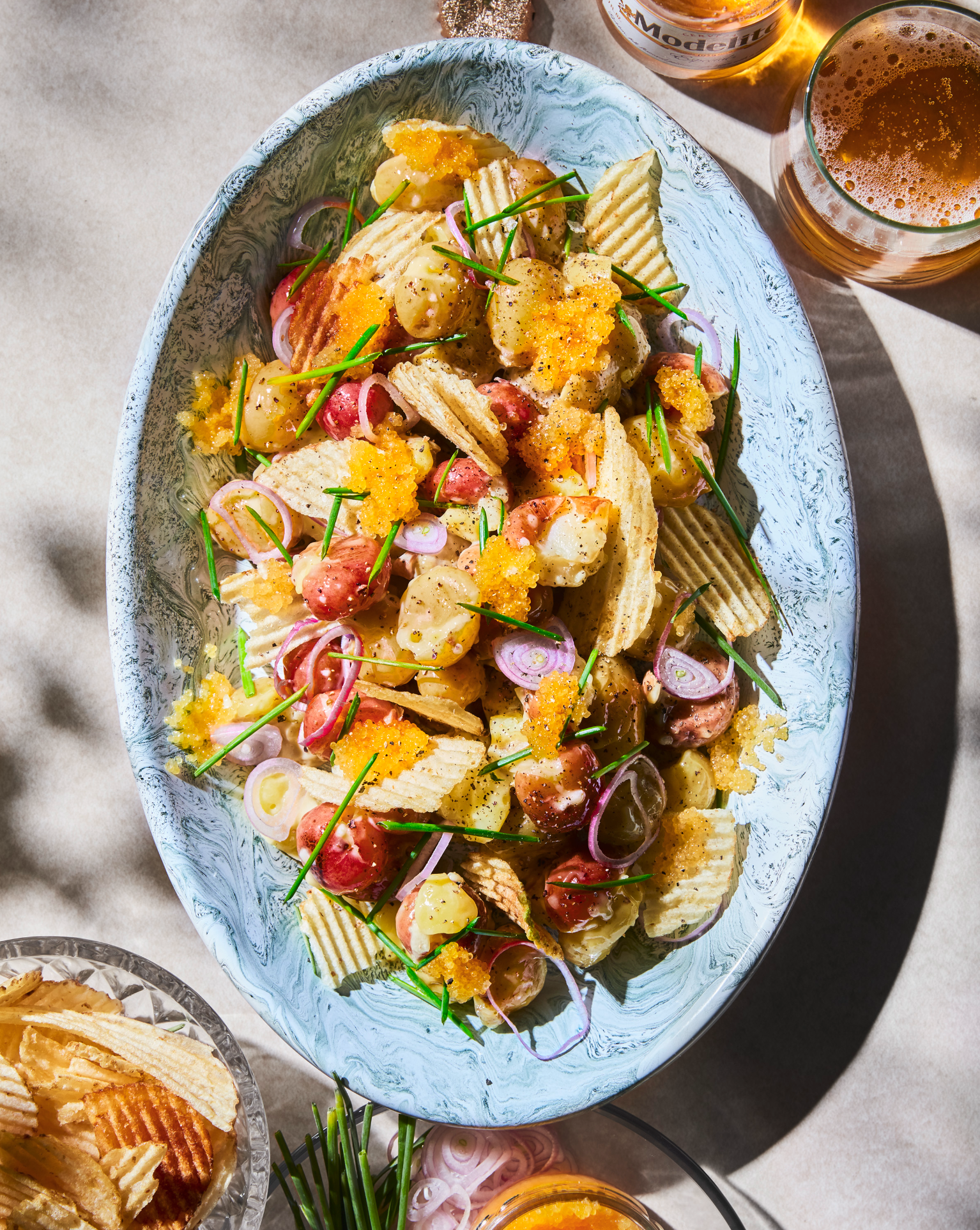 Potato chip salad with cherries, red onions, chives, and a yellow dressing, served on a blue and white oval dish.
