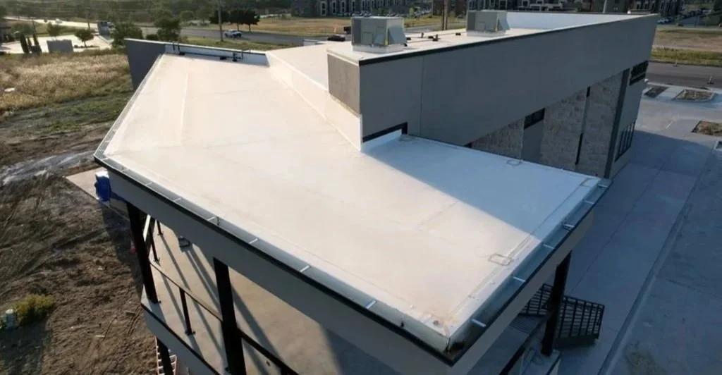 A building with a flat roof and modern architecture, featuring a rooftop HVAC system, located in a partly developed area with some grassy patches and paved walkways.