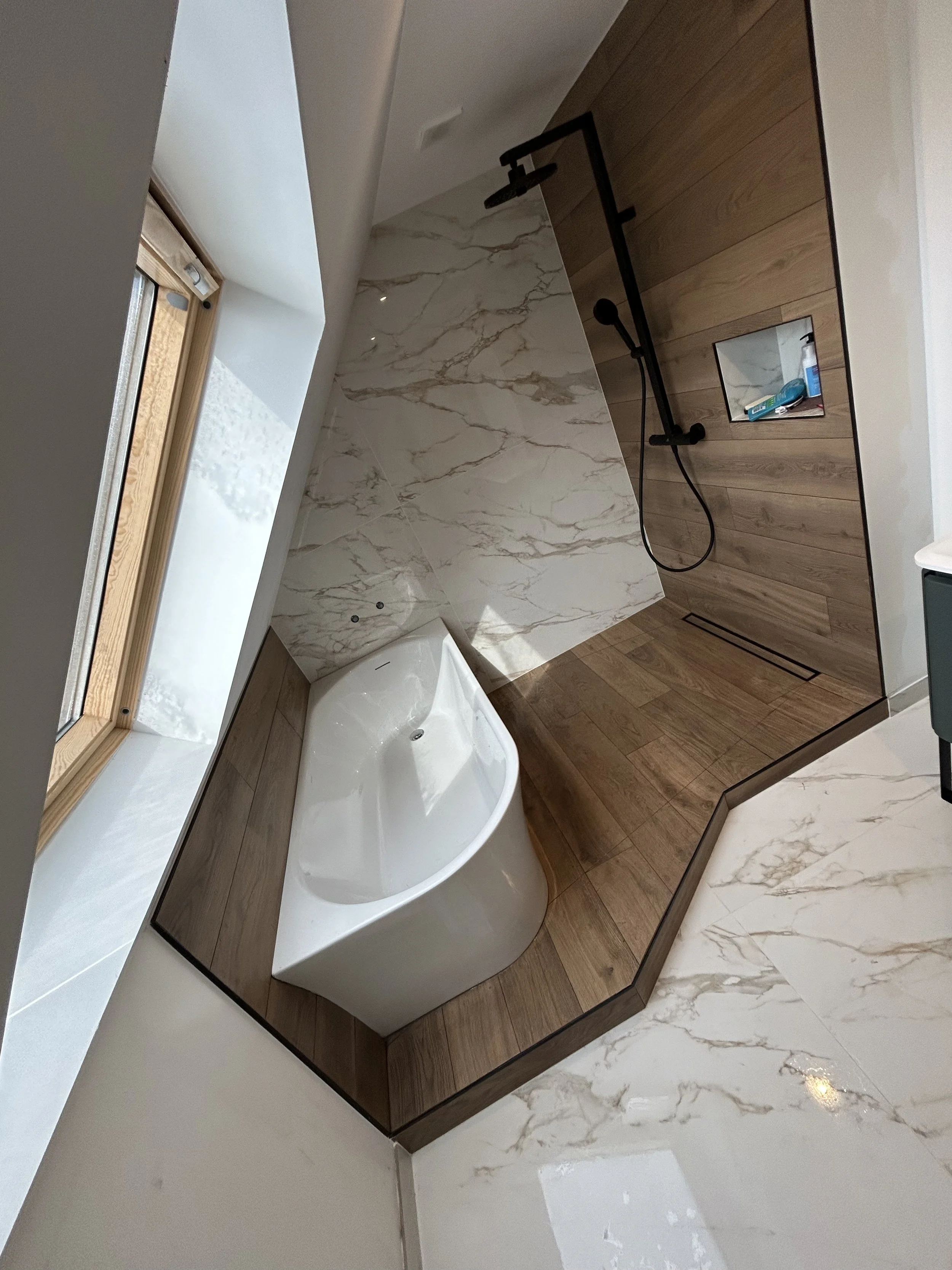 Salle de bain moderne avec une baignoire, douche et revêtement en bois et marbre, vue depuis le sol vers la fenêtre.