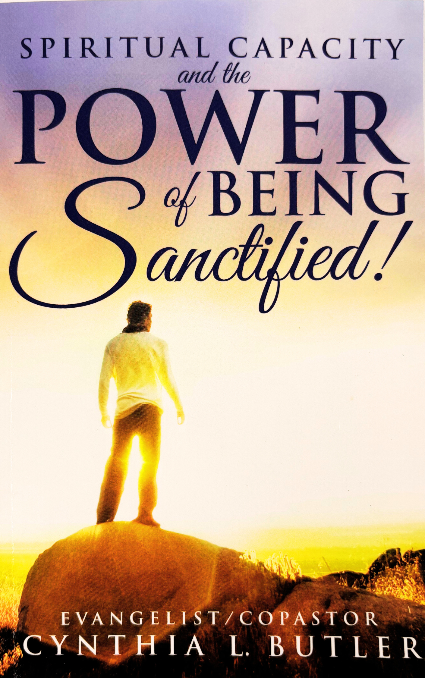 Book cover titled "Spiritual Capacity and the Power of Being Sanctified" by Evangelist/Copastor Cynthia L. Butler, featuring a person standing on a rock looking into a sunset or sunrise over a landscape.