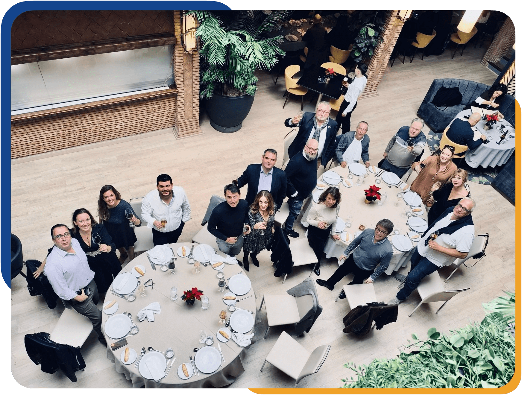 Grupo de personas celebrando en un evento social en un restaurante, con mesas decoradas con flores rojas y comida, algunos levantando copas y sonriendo.