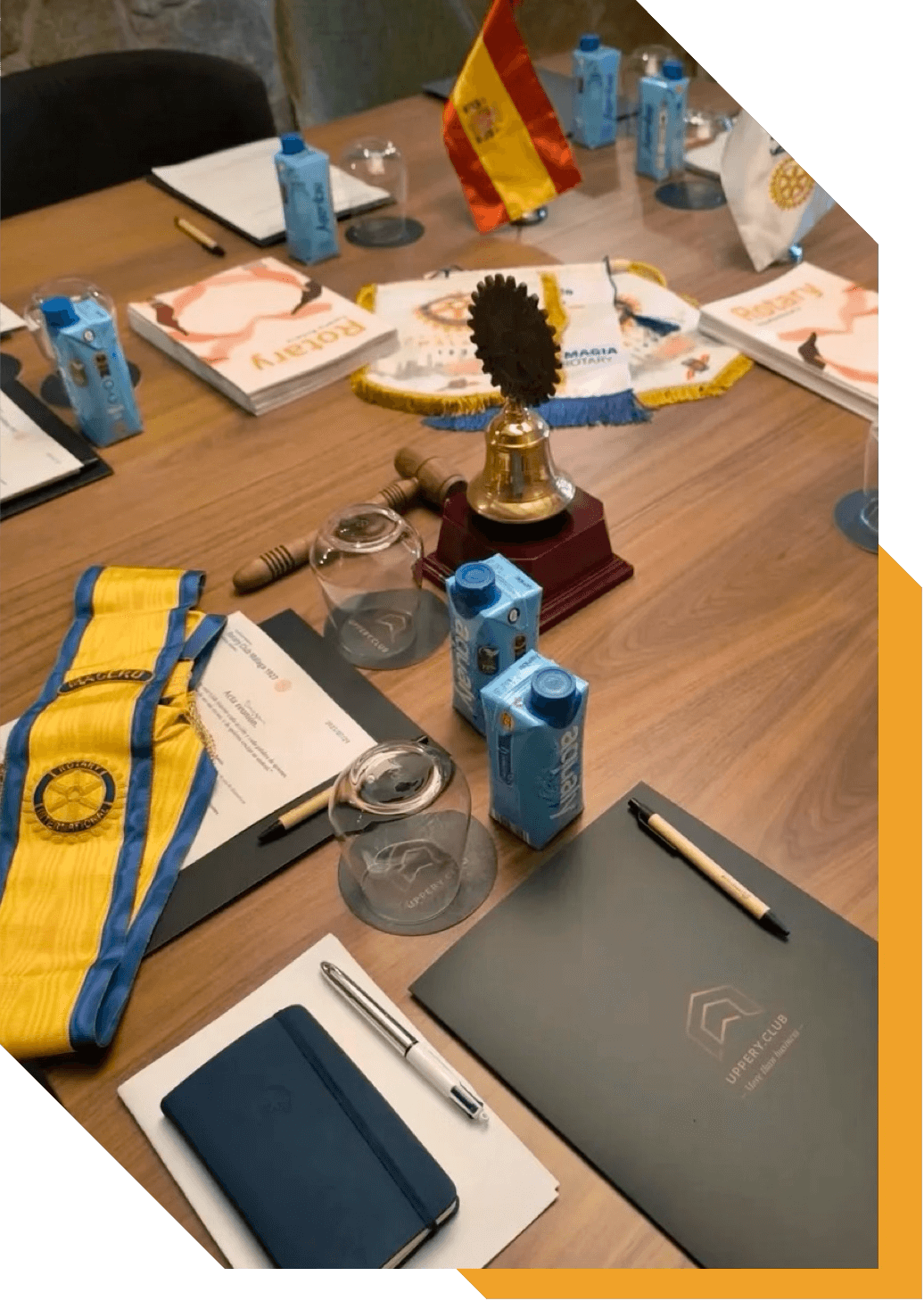 Mesa de reuniones con documentos, libretas, bolígrafos, botellas de jugo, banderas y un trofeo al centro.