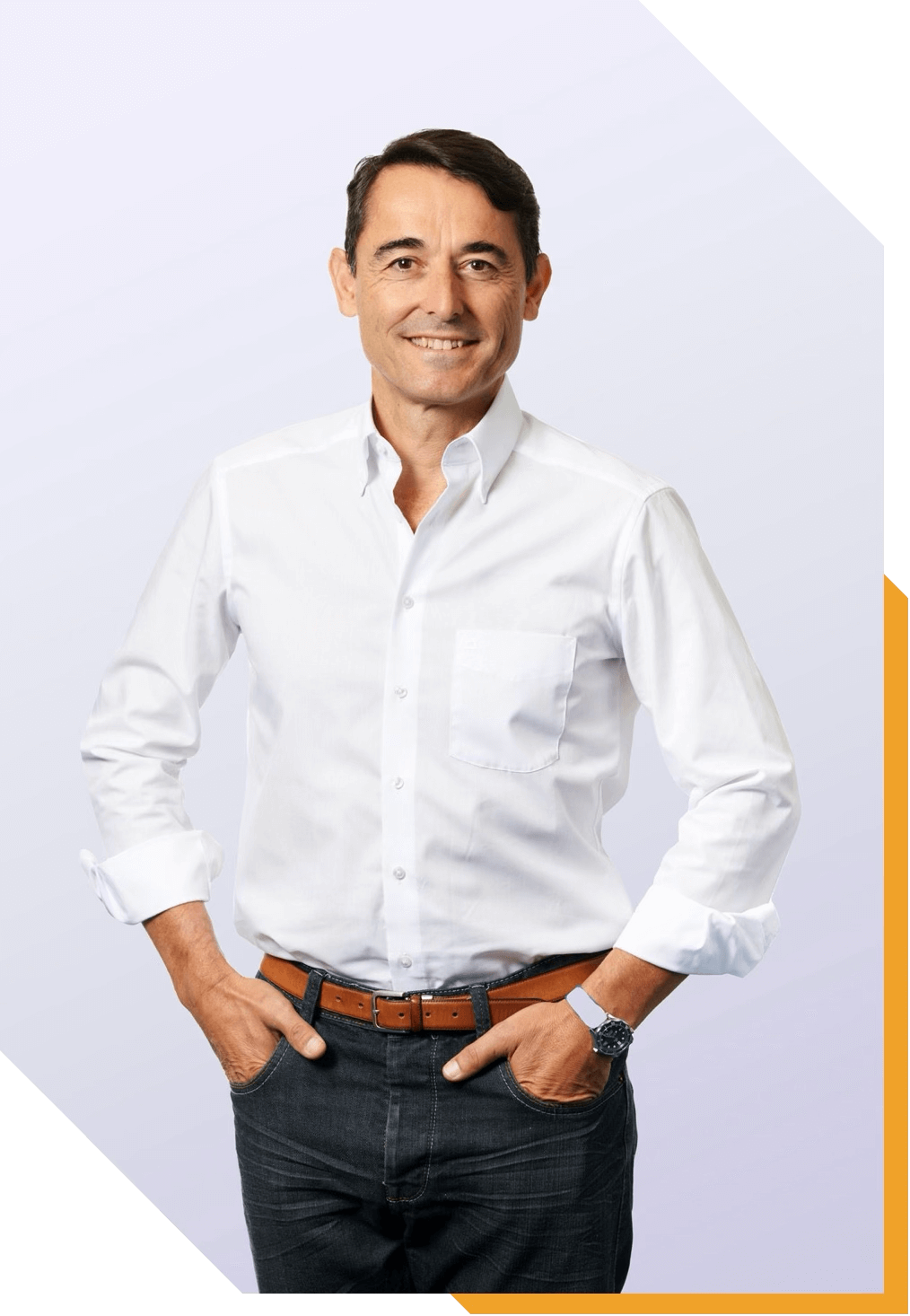 Hombre sonriendo, con camiseta blanca y pantalones oscuros, en un fondo claro.