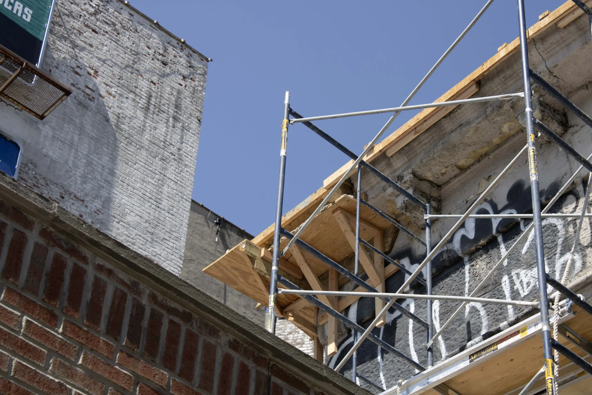 Exterior condition of left side of arch with temporary scaffolding set up to support cornice and erase graffiti.