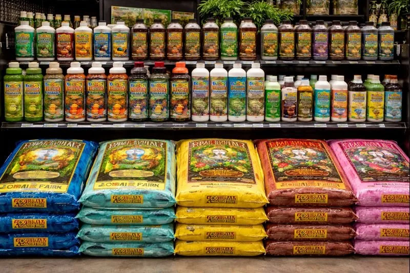 Display of various gardening products, including bottles of plant fertilizer and bags of potting soil, on store shelves.