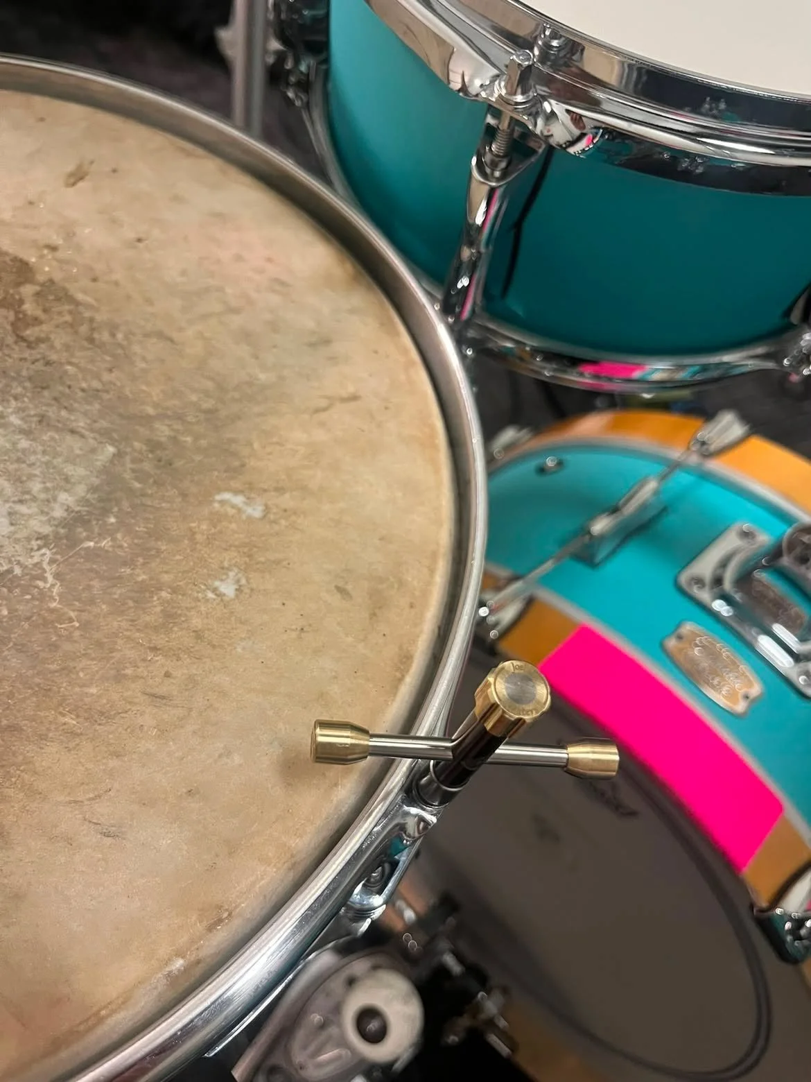 Close-up of a vintage drum set with colorful shells and a weathered drumhead and DG custom drum key. Anubis 