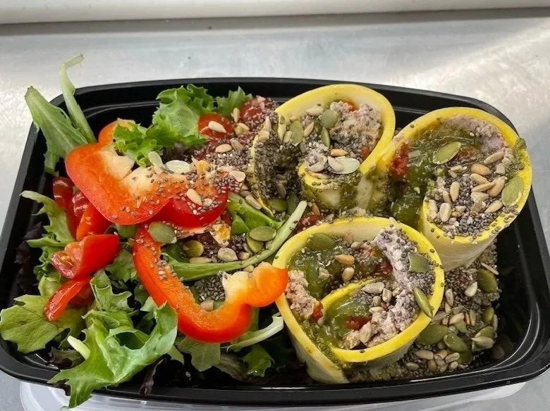 Salad with red and orange bell peppers, lettuce, and stuffed zucchini boats topped with seeds and herbs.
