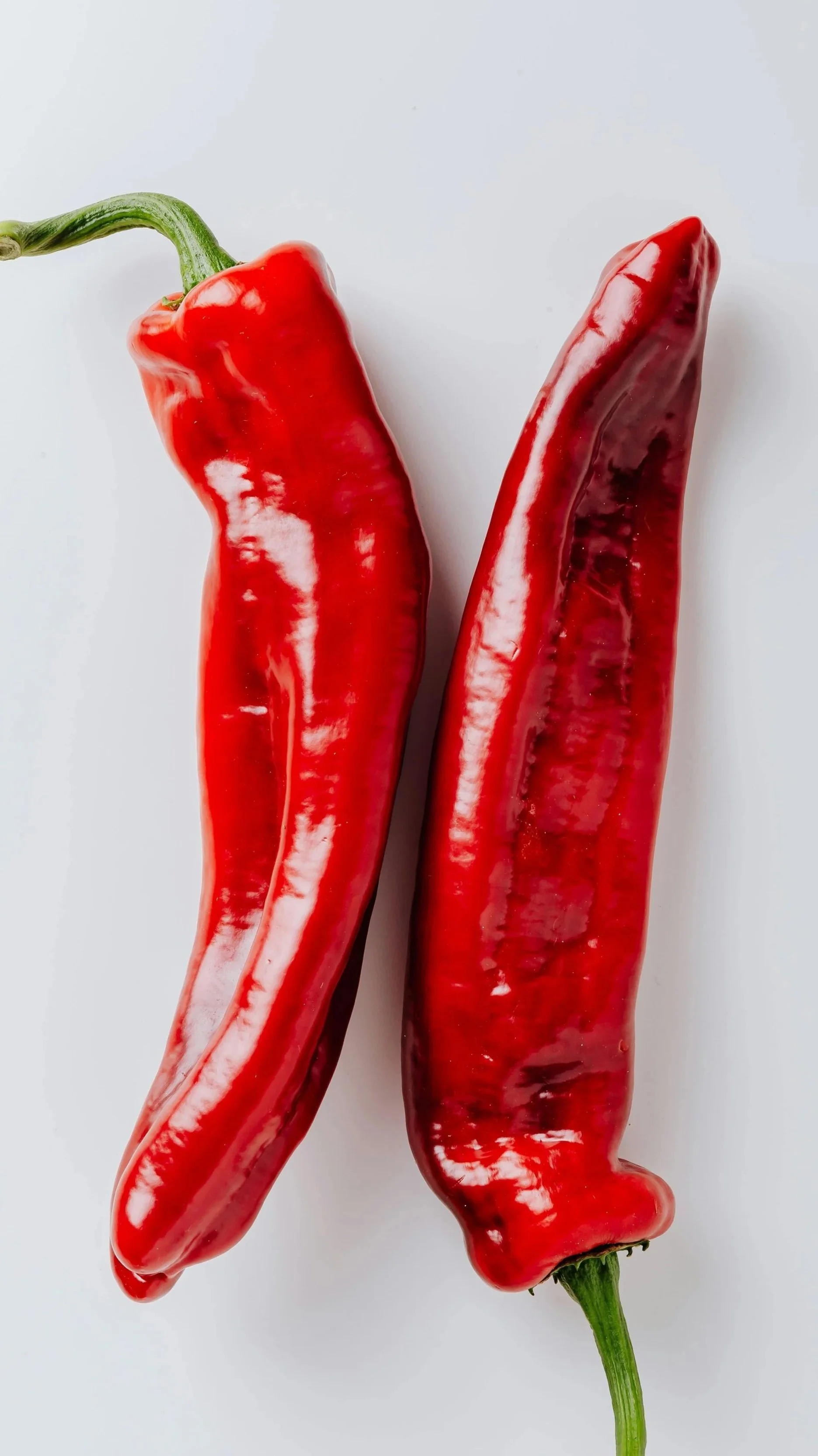 Two red chili peppers with green stems on a white background.
