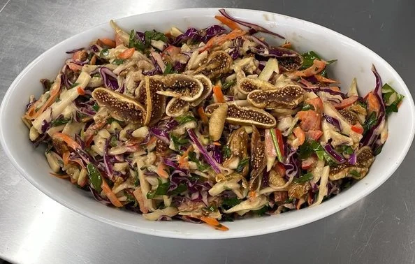 Vegetable salad with purple cabbage, carrots, and sliced figs in an oval white dish.