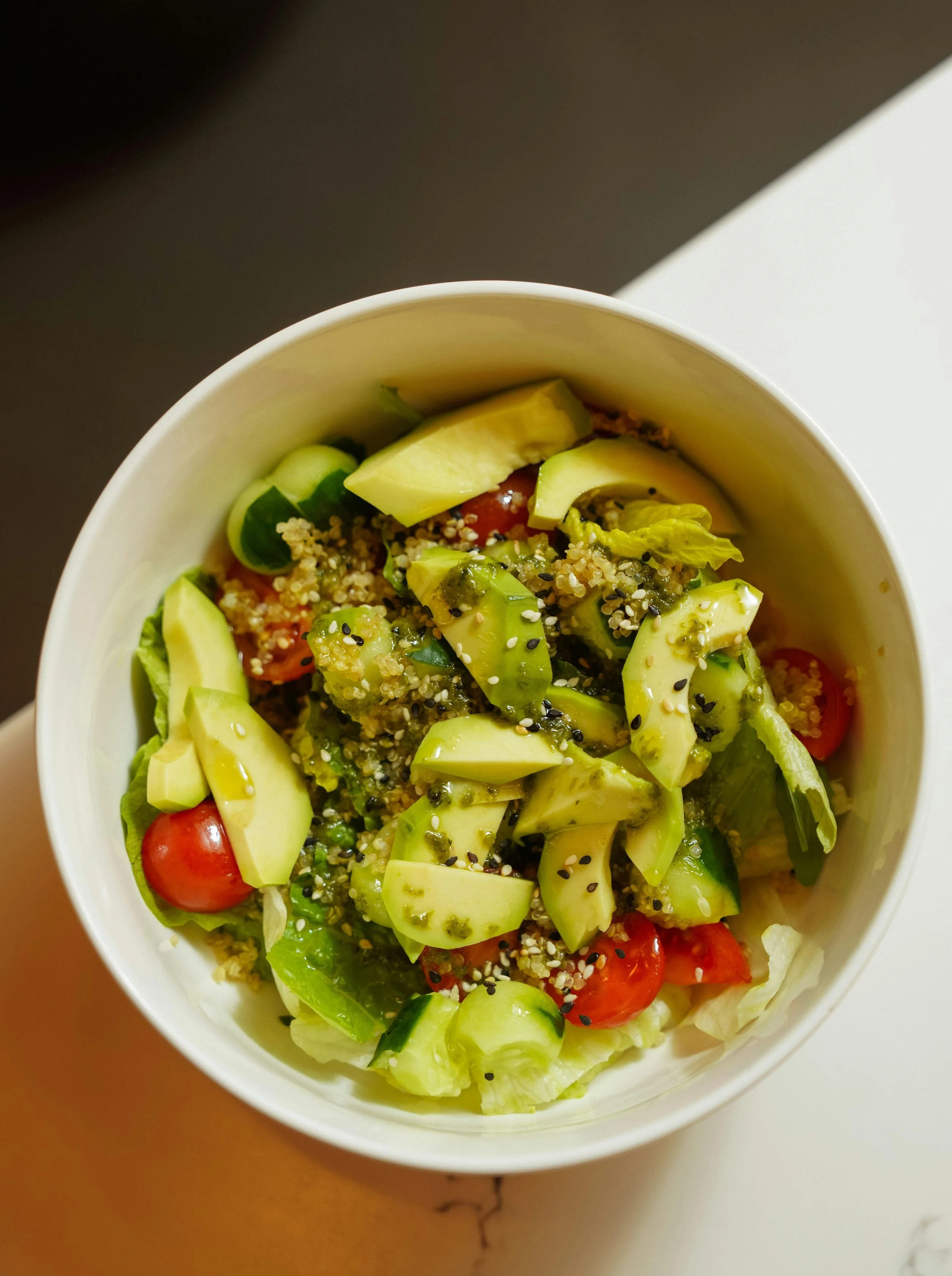 Fresh vegetable salad with cherry tomatoes, avocado, cucumbers, lettuce, and sprinkled seeds in a paper bowl.