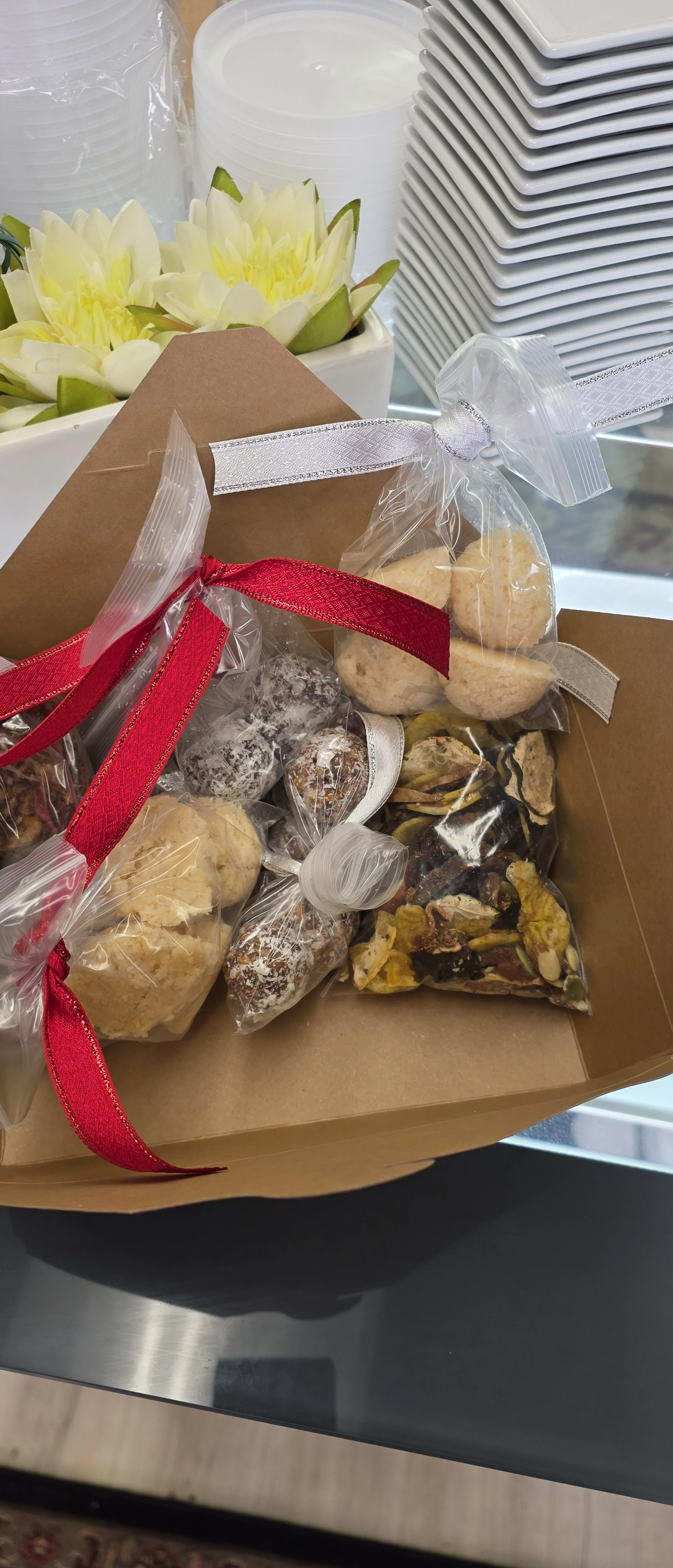 A gift box with assorted cookies wrapped in clear plastic and tied with red, silver, and white ribbons, placed on a glass surface.