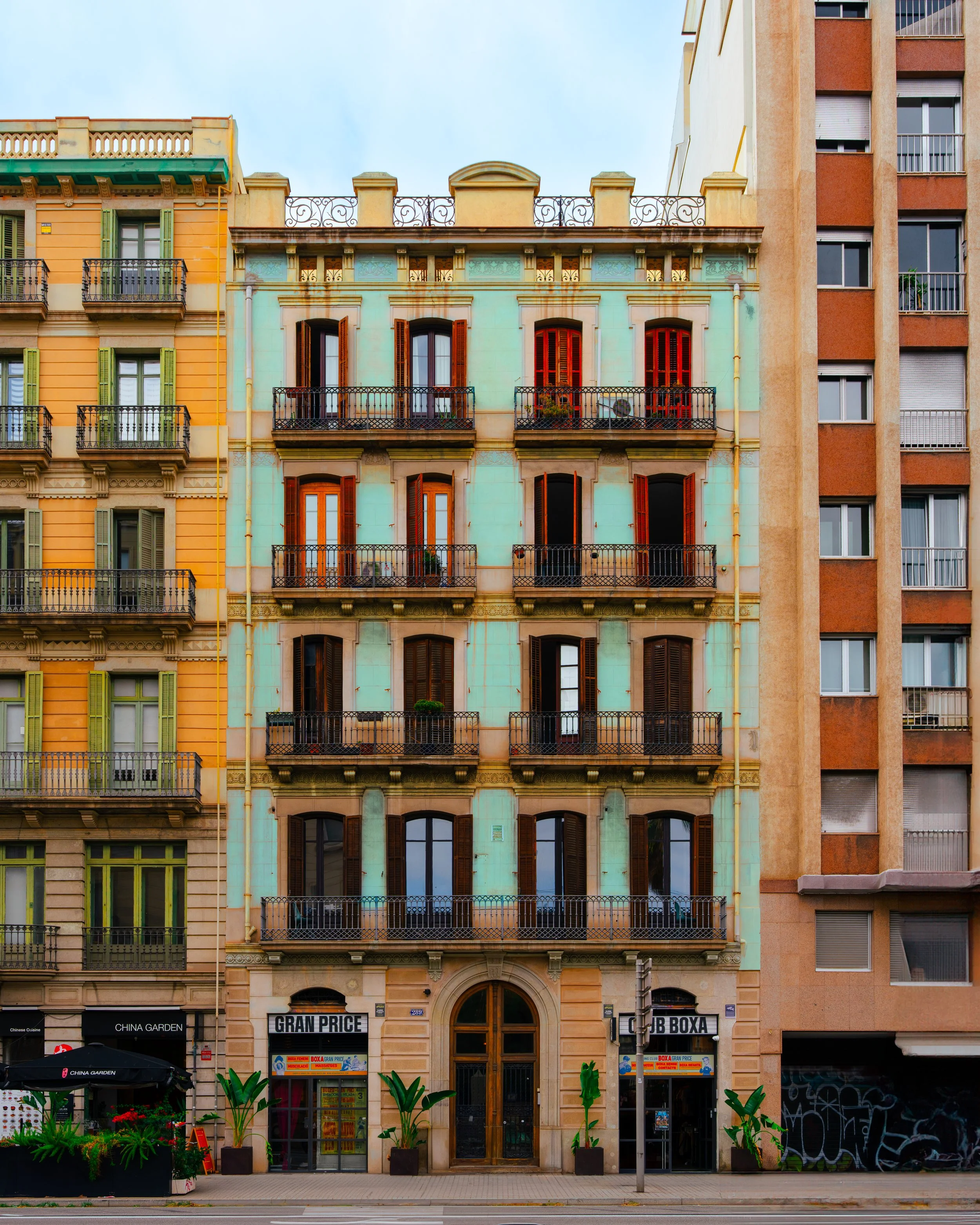 Colorful multi-story residential building with balconies, wooden shutters, and ground-floor shops in an urban setting.