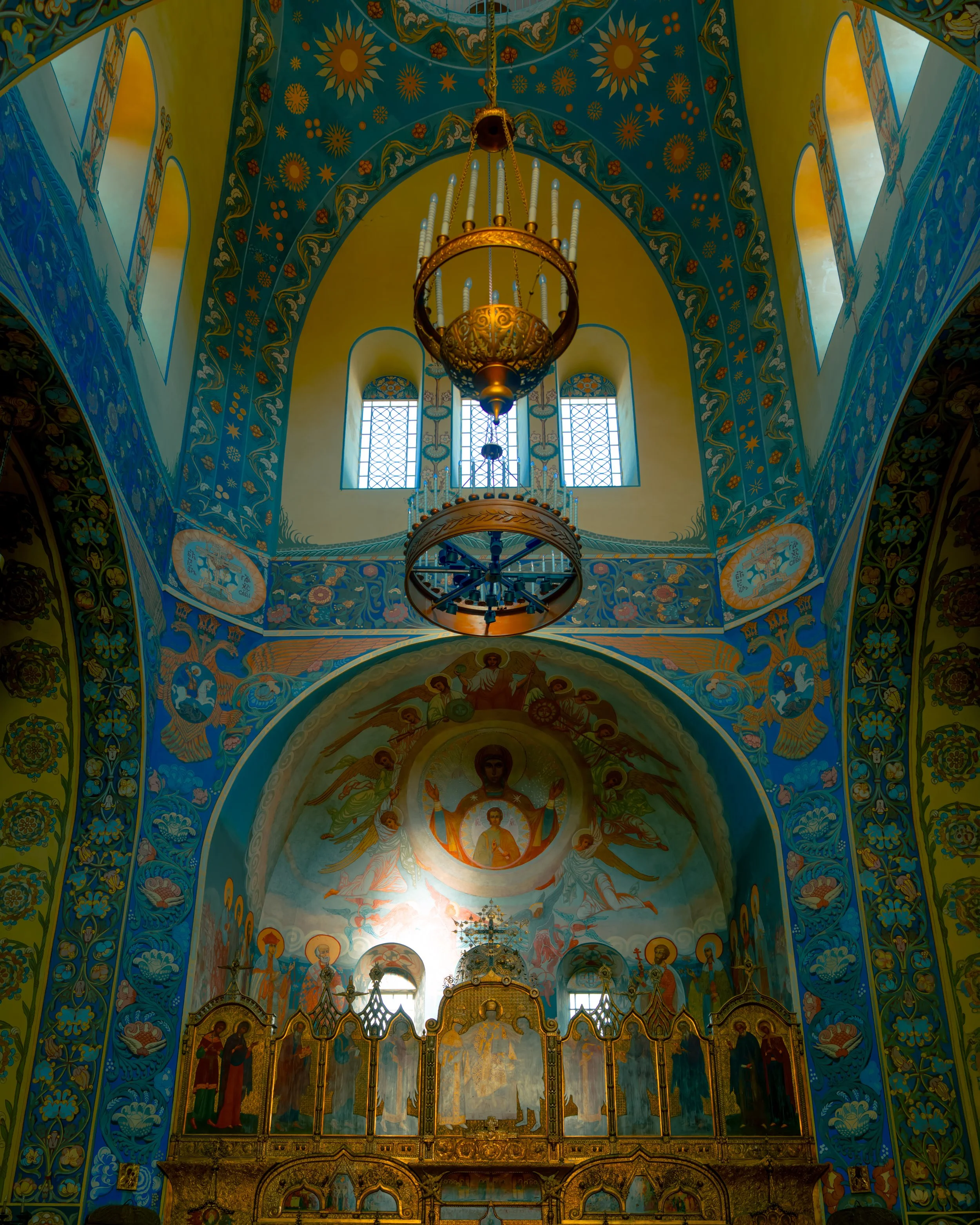 Interior of an ornately decorated Eastern Orthodox church with a painted ceiling, religious icons, and a chandelier.