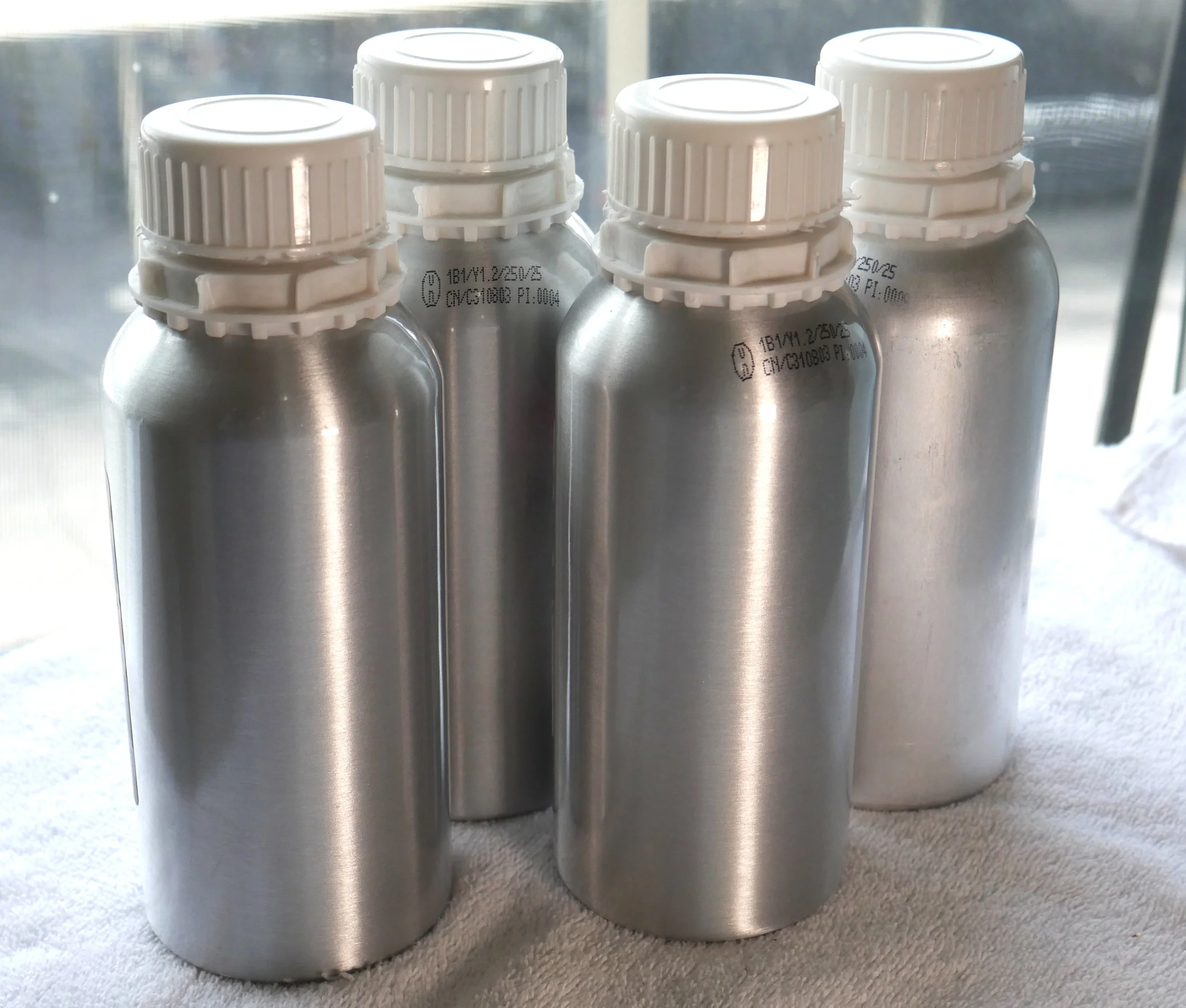 Multiple small glass bottles filled with golden liquid, some with cork stoppers and one with a rounded wooden dropper, sitting on a wooden surface with spilled drops of oil.