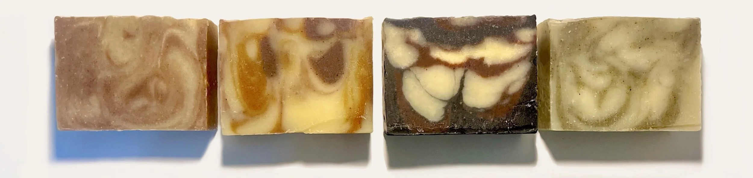 Four handmade soap bars with swirled, marbled patterns in different colors arranged in a row on a white background.