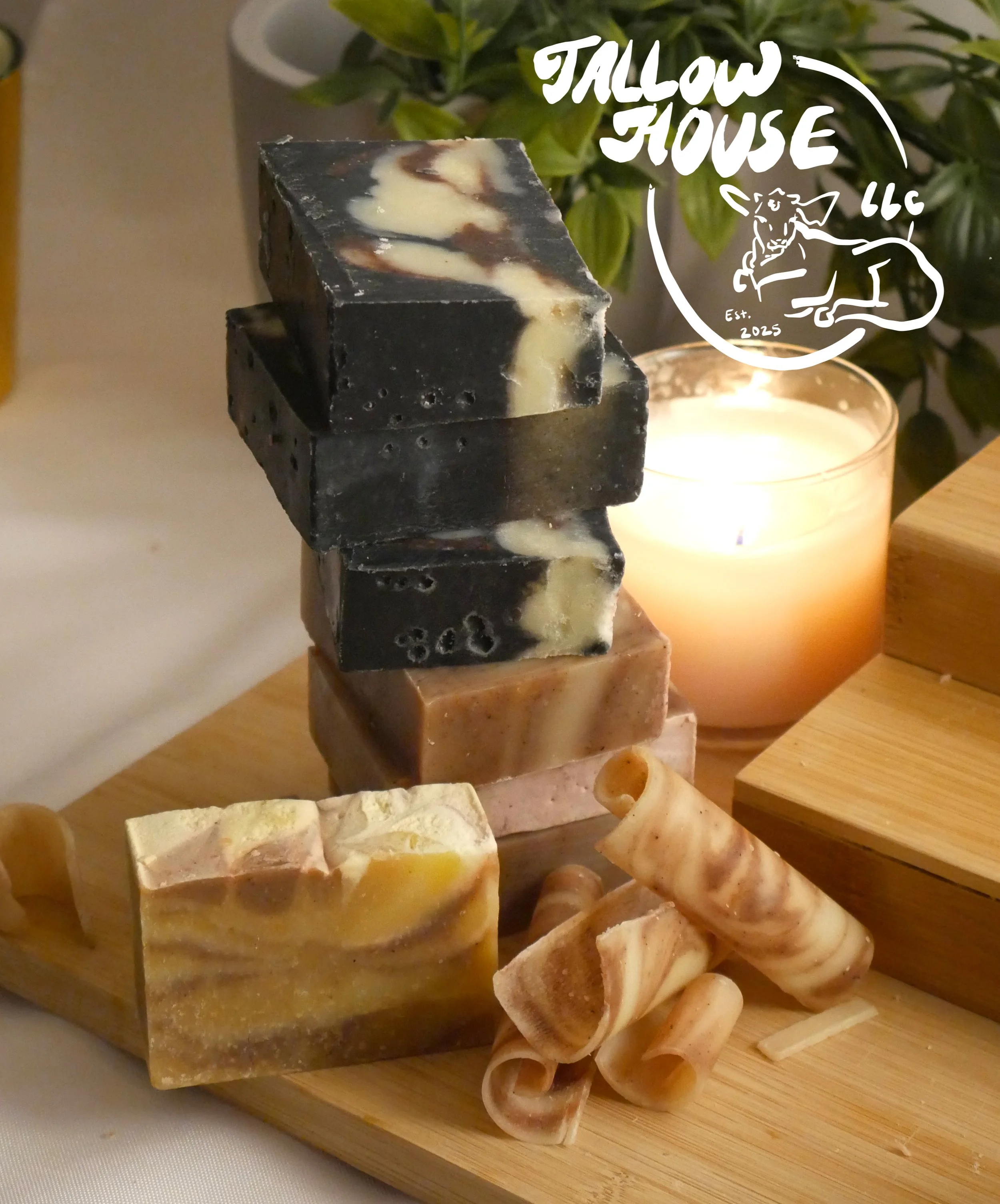 Stack of artisanal soap bars and soap curls on a wooden board with a lit candle and a green plant in the background.