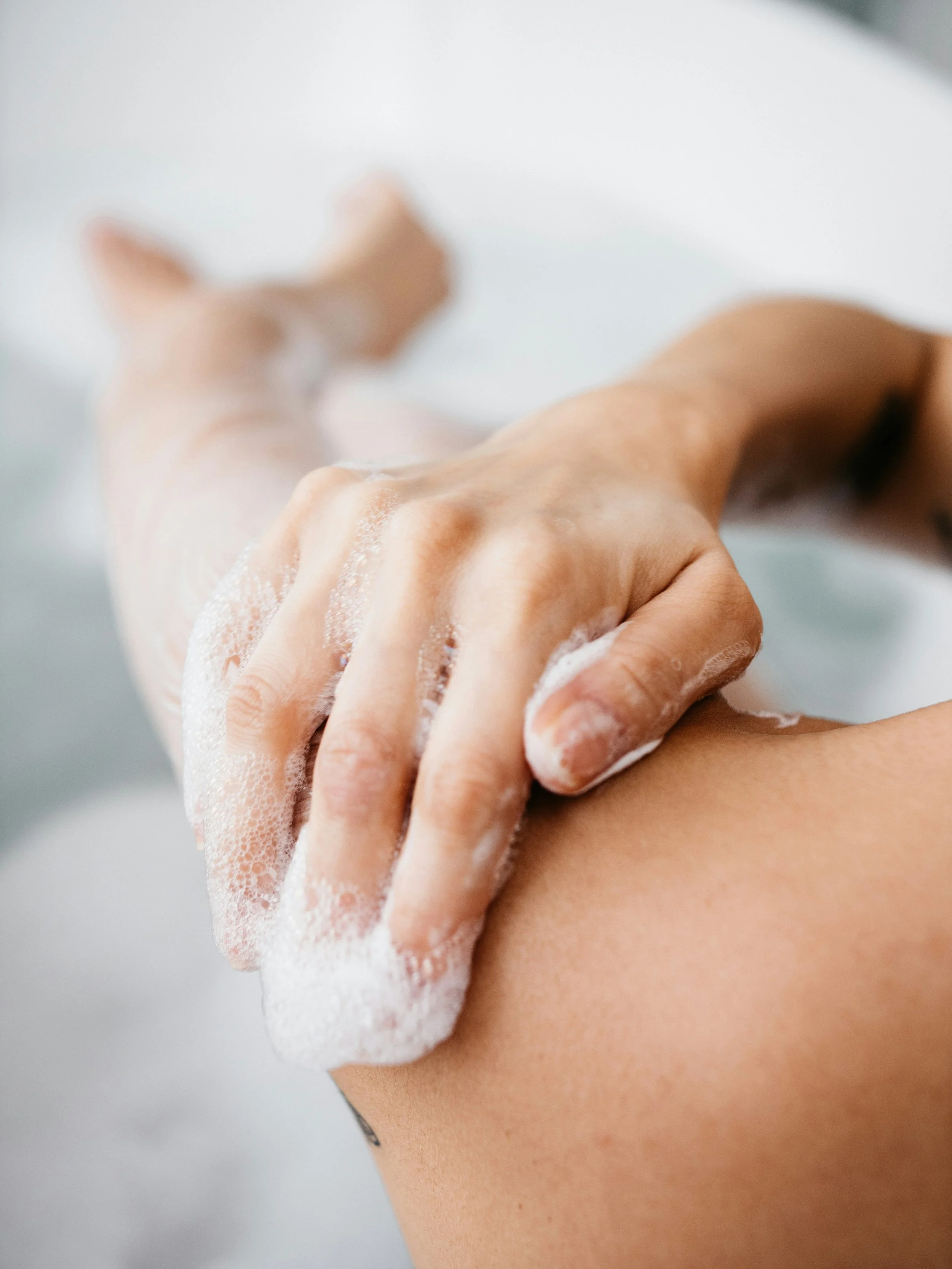 Close-up of a person applying soap and lathering in the shower, focusing on their hand and shoulder.