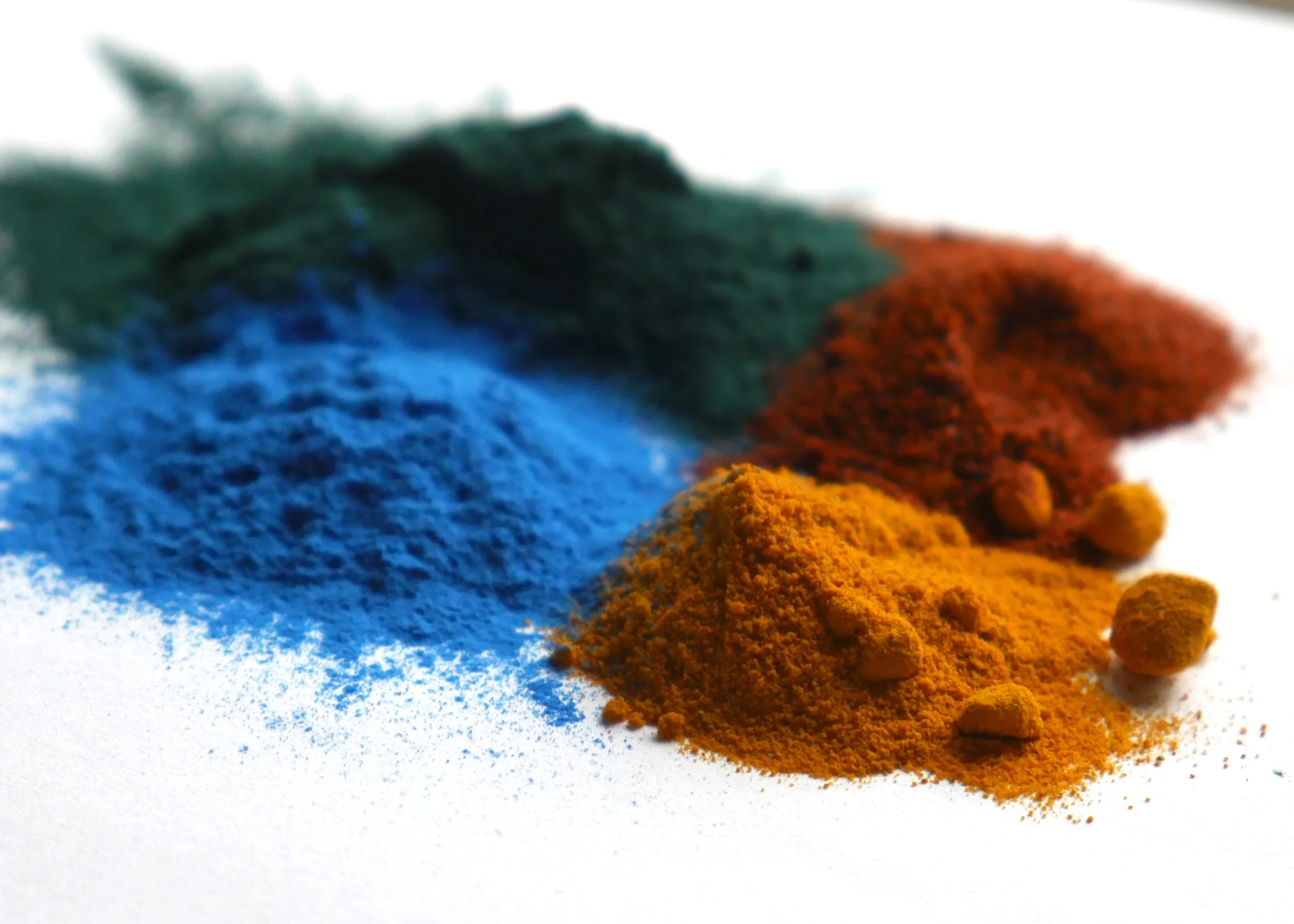 Close-up of four different powders: top-left dark brown dry ground coffee; top-right bright yellow turmeric powder; bottom-left reddish-brown cinnamon powder; bottom-right yellow curry powder with small bits of herbs.