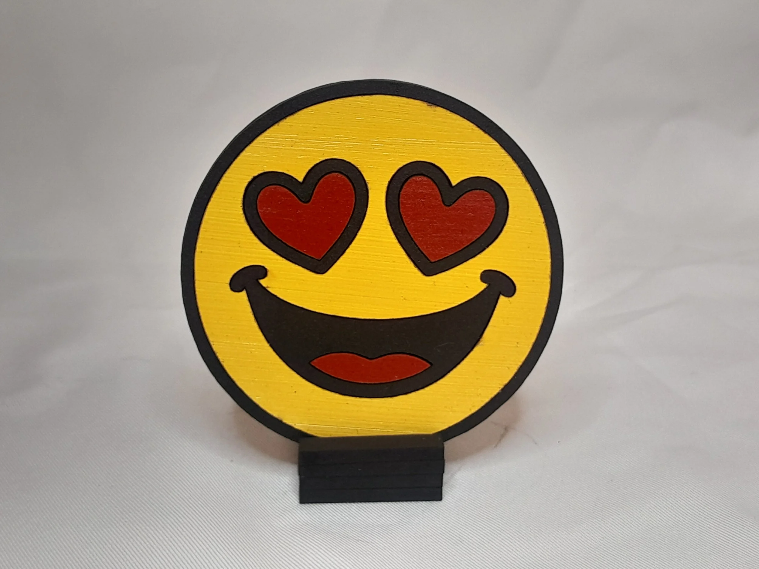 “Classic yellow heart eyes emoji magnet in Fun Style, laser‑cut painted wood with bold black outlines, displayed on a wooden easel.”