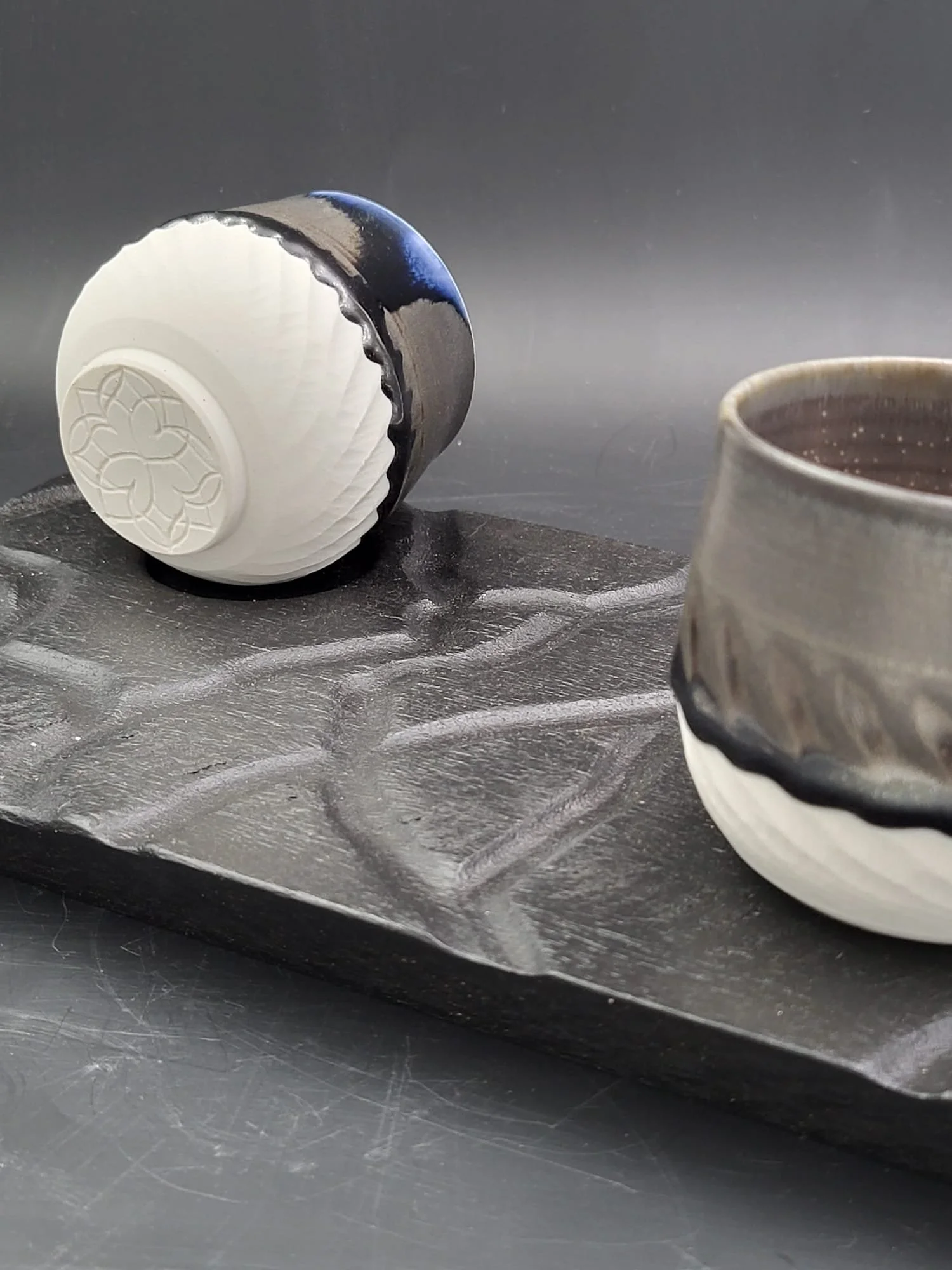 Two ceramic cups with black and white designs on a textured black tray against a dark background.