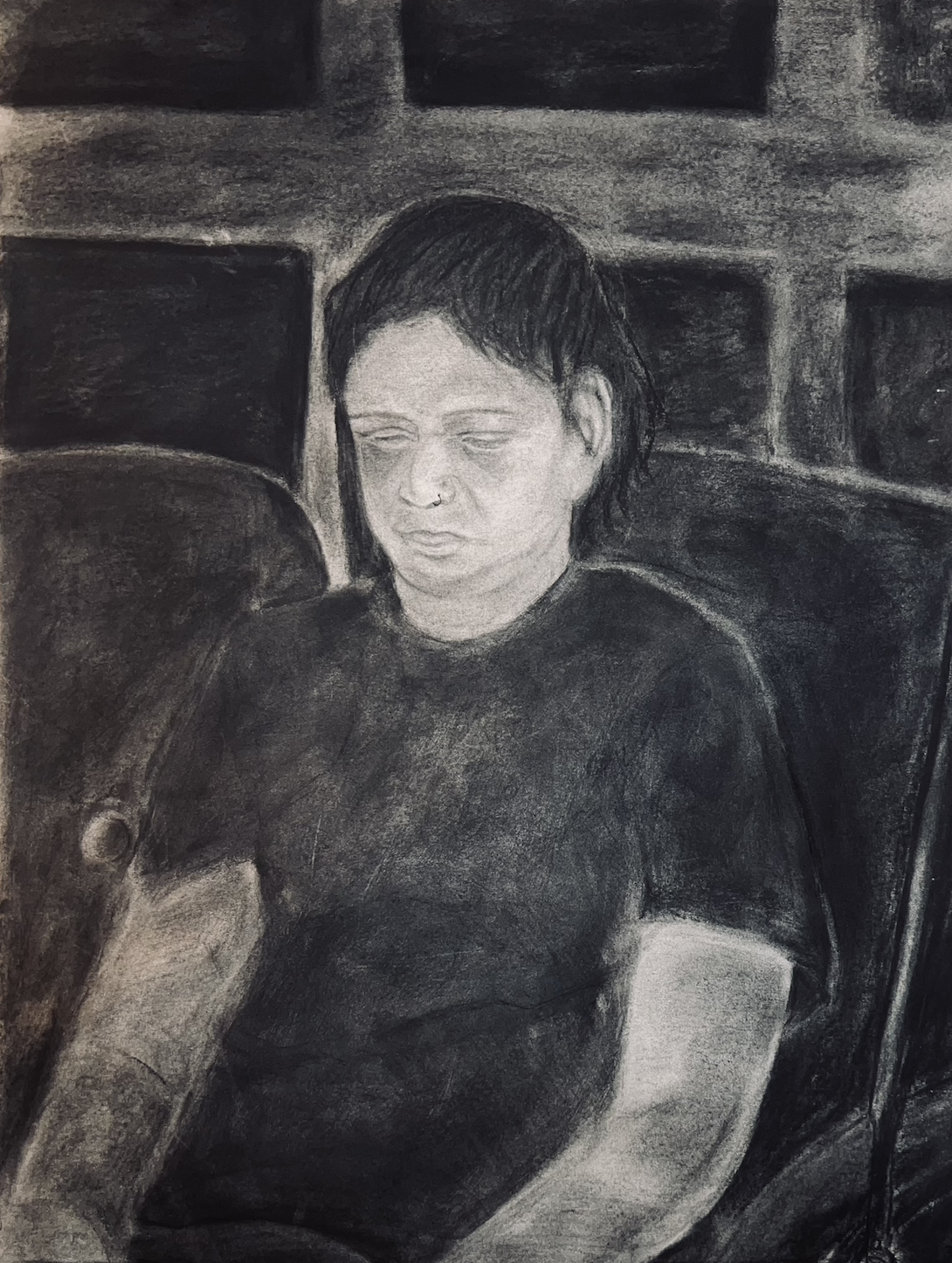 A person with dark hair and a nose ring, looking down.