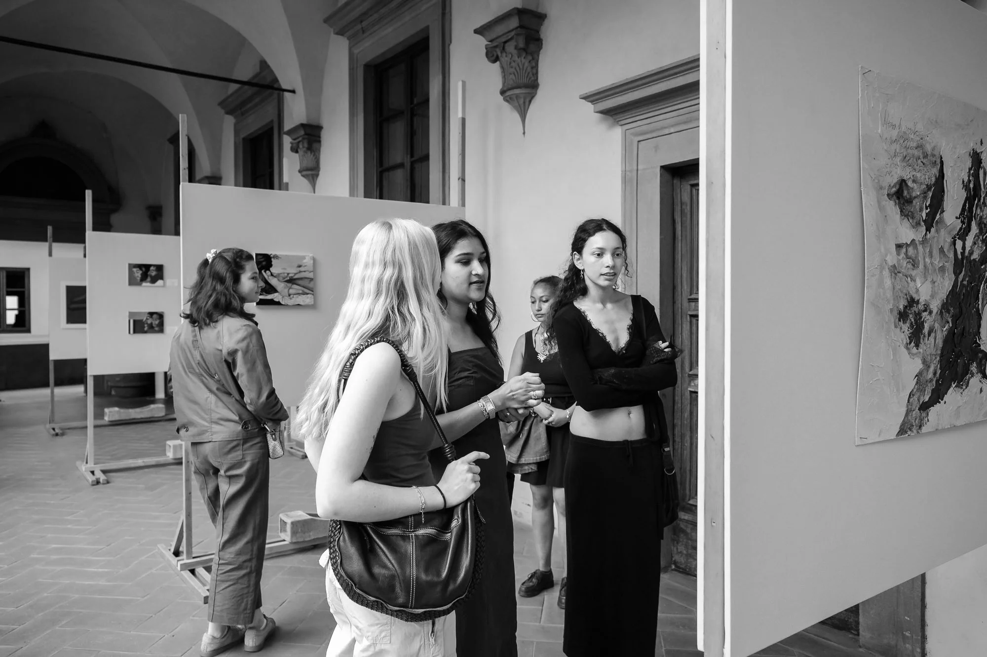 A group of five women at an art gallery, looking at a large abstract painting on the wall. The women are engaged and observing the artwork attentively.