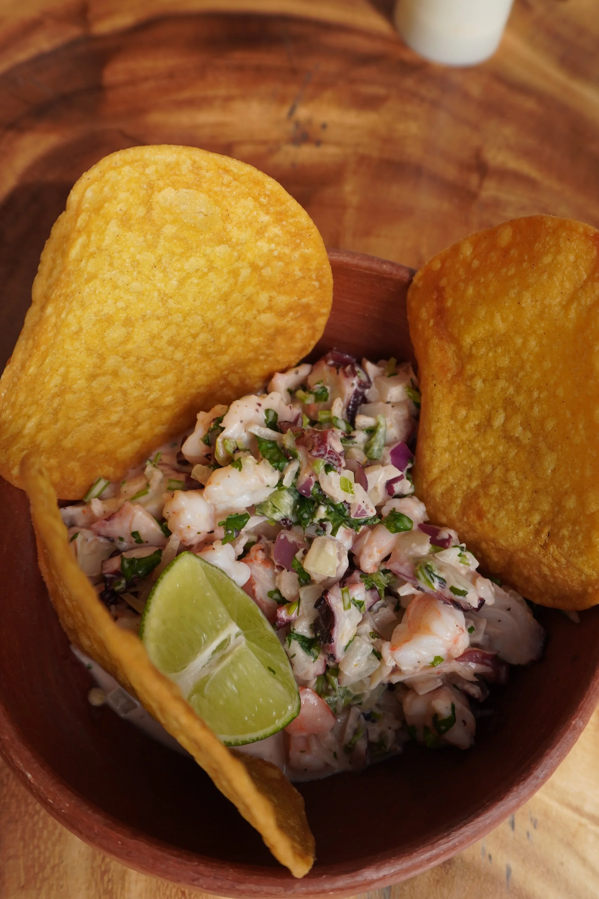 A bowl of seafood ceviche with lime wedge and two tortilla chips.