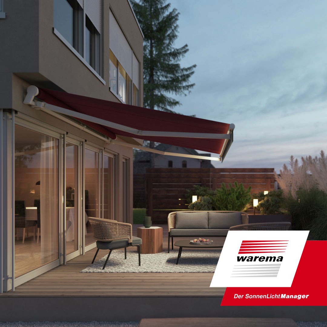 Modern outdoor patio with wicker and cushioned seating, a coffee table with snacks, and a dining area inside a house with large sliding glass doors. A red retractable awning provides shade, and there are exterior lights and greenery in the background